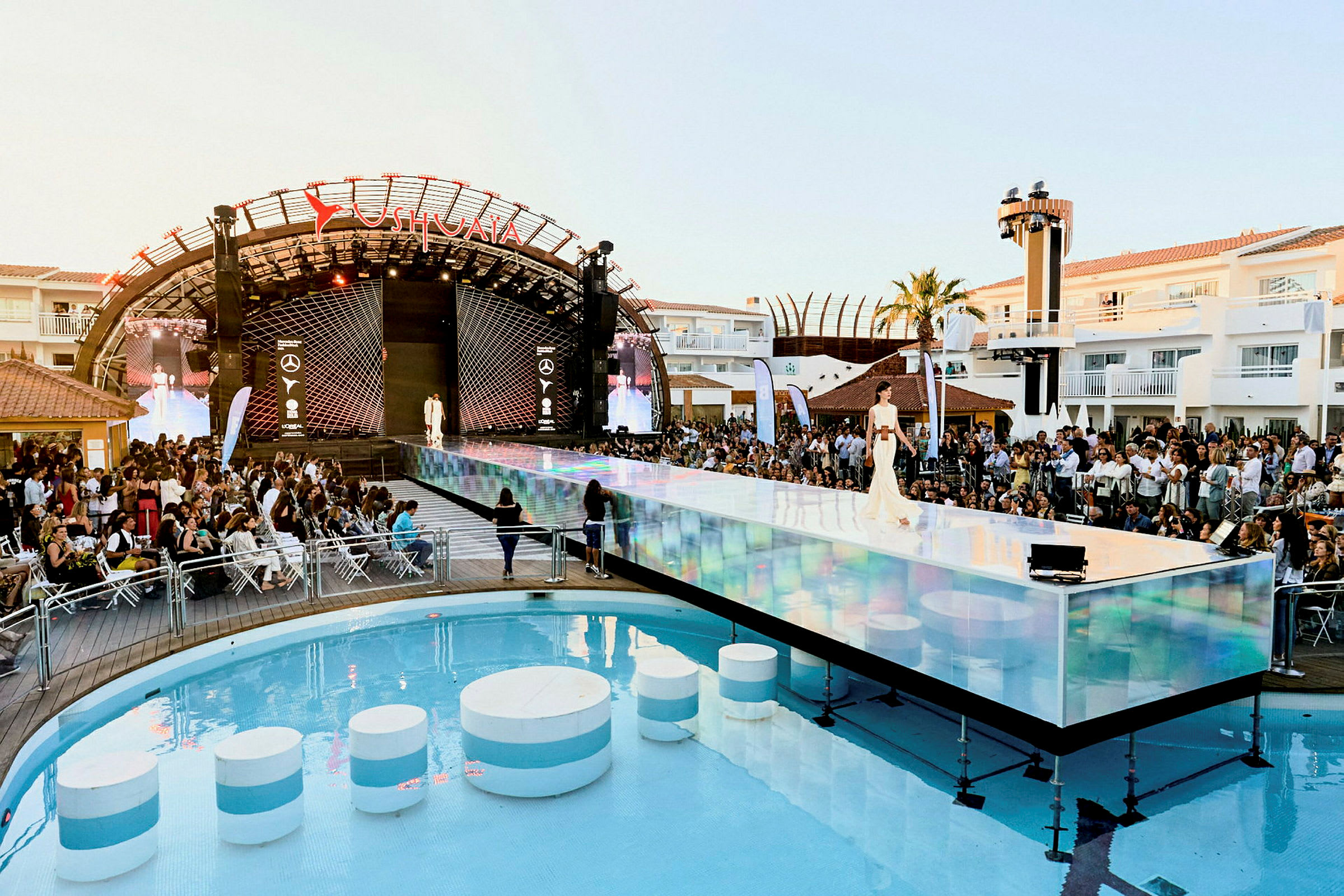 Et modeshow med en catwalk over en swimmingpool og et publikum i baggrunden. (AI-genereret tekst)