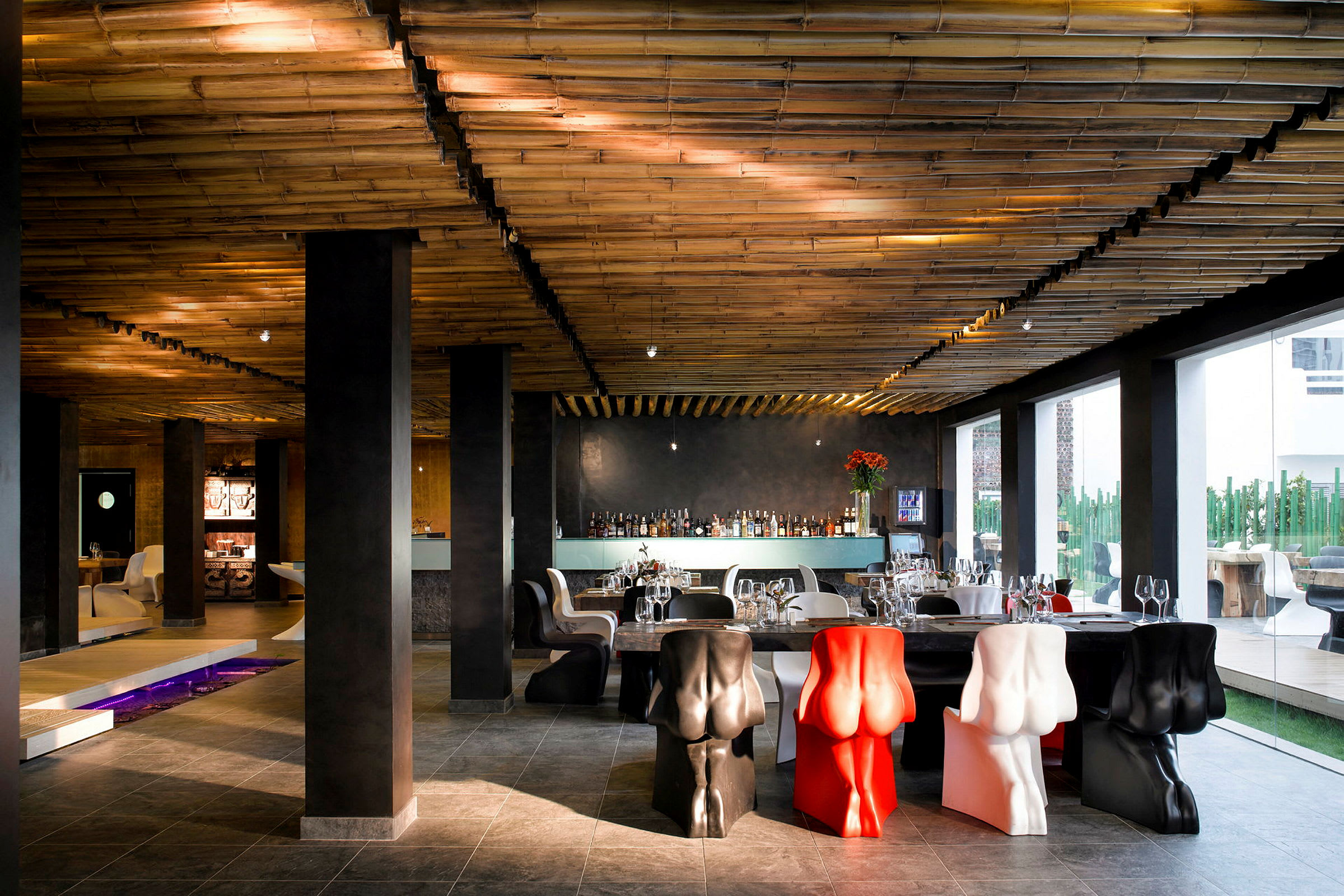 Restaurant med dekorative stole, et bambustag og store vinduer, der lader lys komme ind. (AI-genereret tekst)