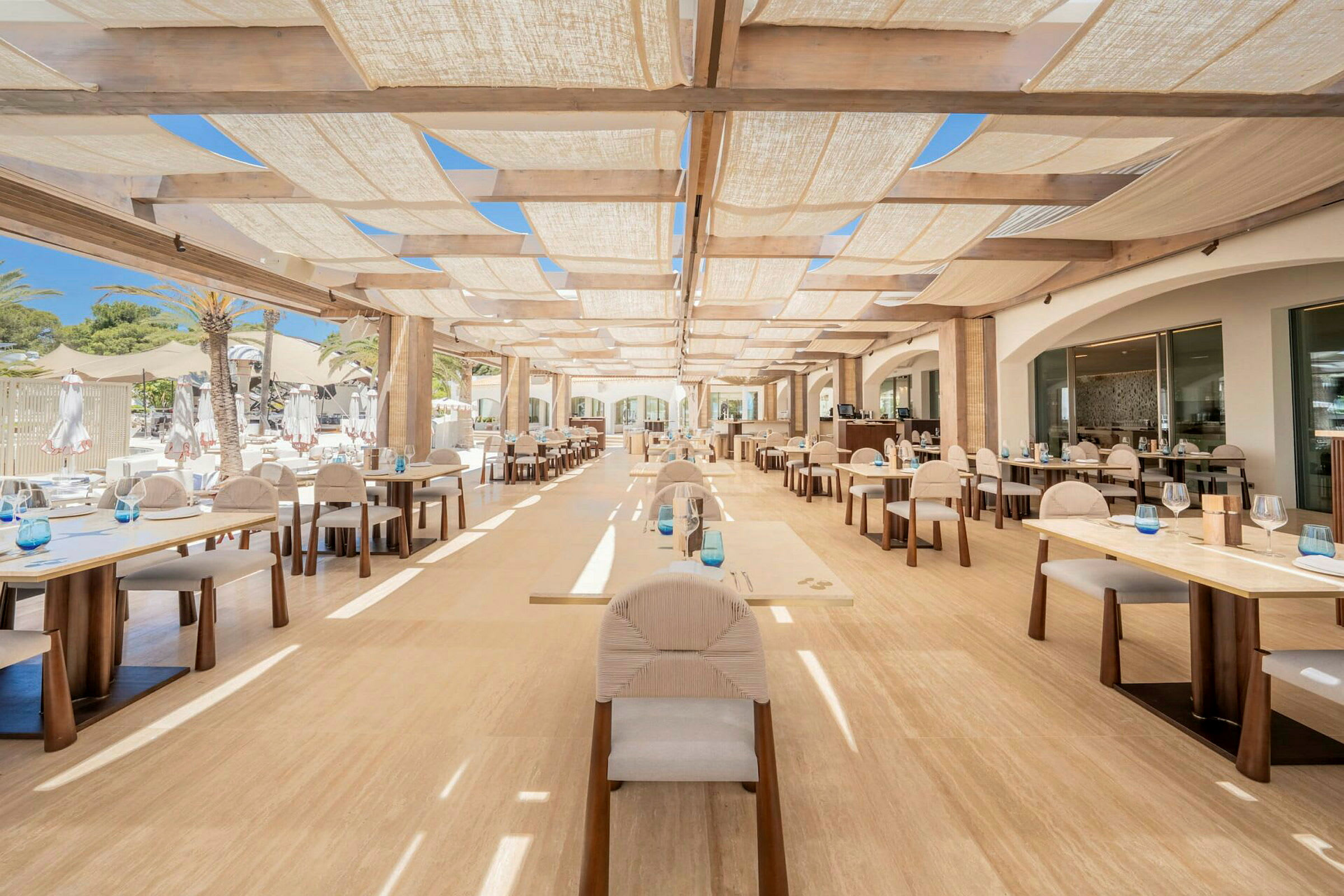 En udendørsrestaurant med borde og stole under et skyggefuldt tag. (AI-genereret tekst)