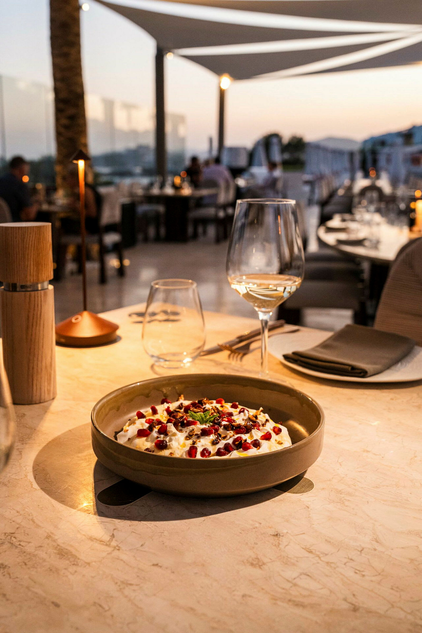 En tallerken med mad, et vinglas og bordtilbehør på et elegant dækket bord, med baggrunden, der viser en restaurantstemning ved skumringen. (AI-genereret tekst)