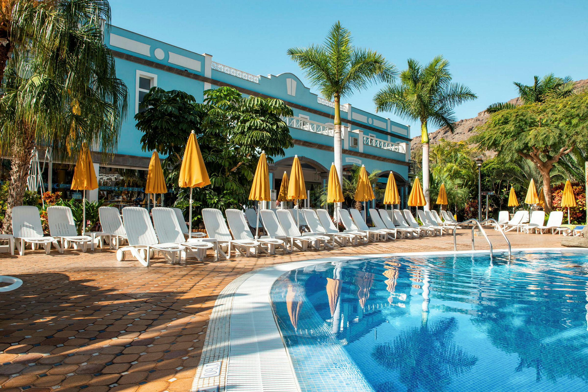 Udendørs pool ved et hotel med liggestole og gule parasoller. (AI-genereret tekst)