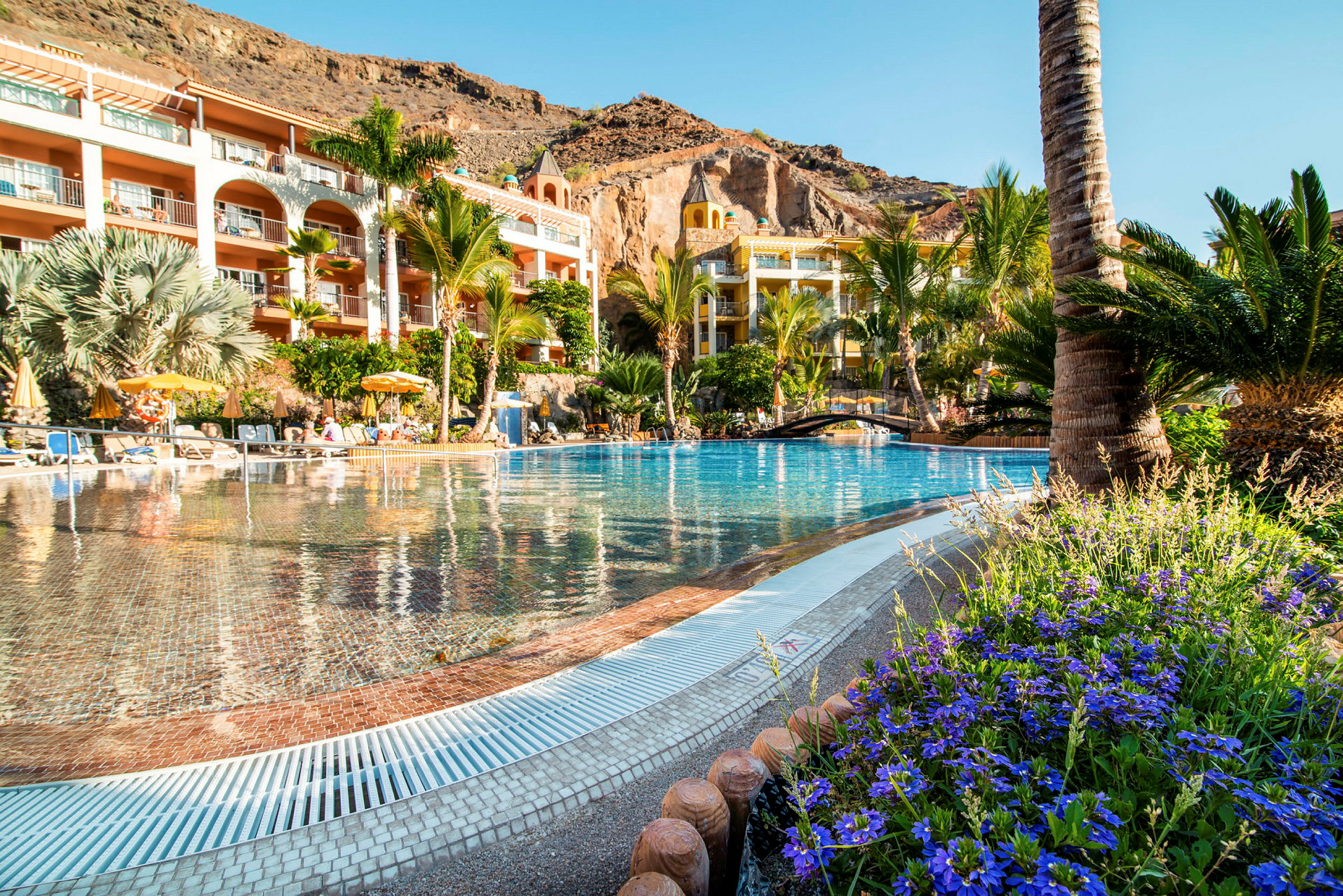 Et billede af en pool ved et hotel omgivet af grønne områder og bjerge. (AI-genereret tekst)