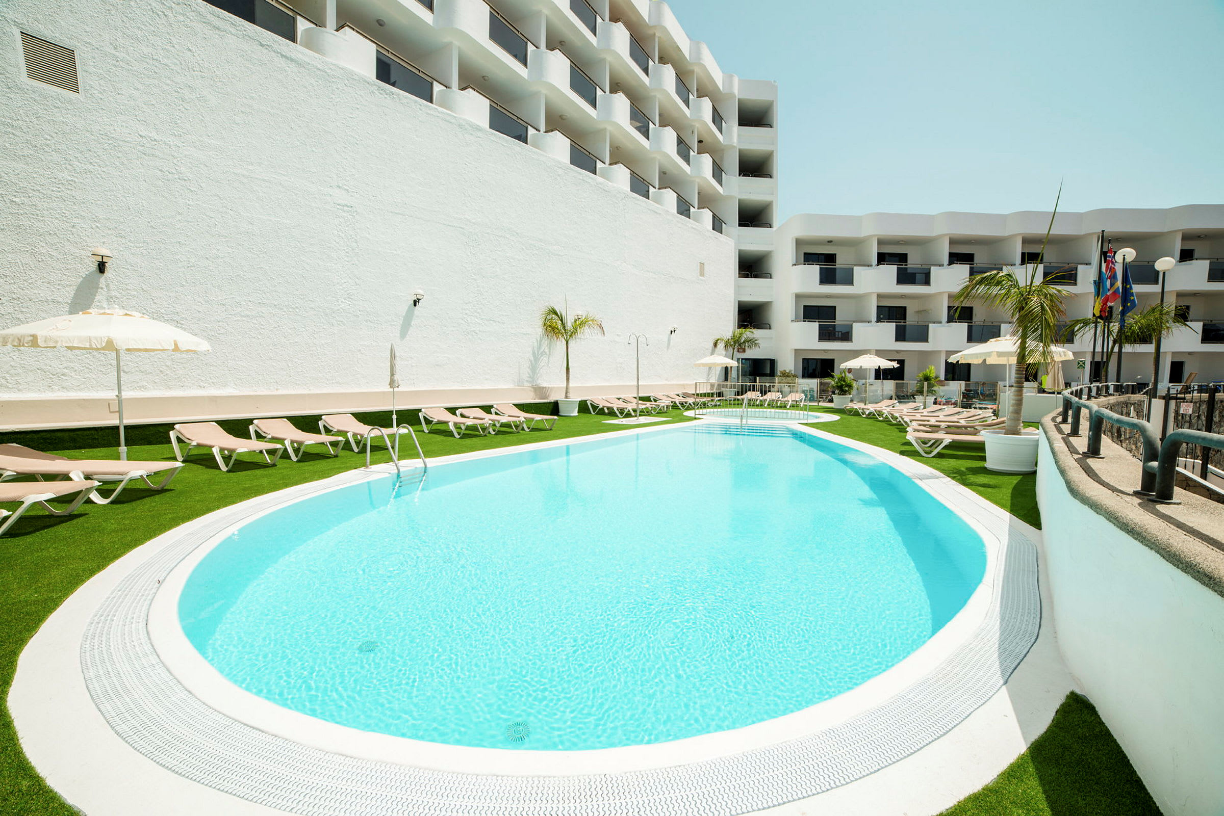En hotelpool omgivet af liggestole og parasoller. (AI-genereret tekst)
