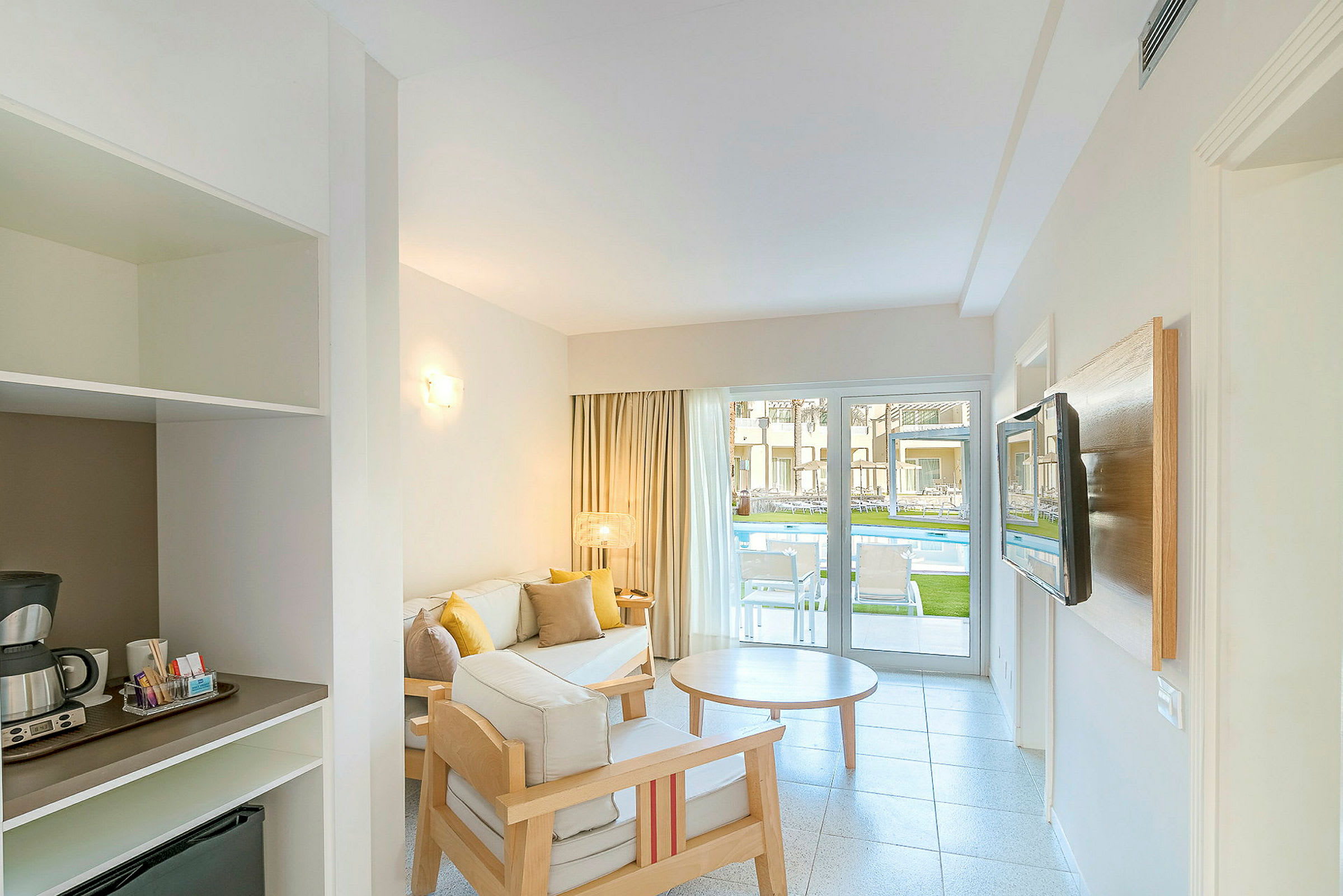 Hotelværelse med siddeområde og udsigt til poolen gennem en glasdør. (AI-genereret tekst)