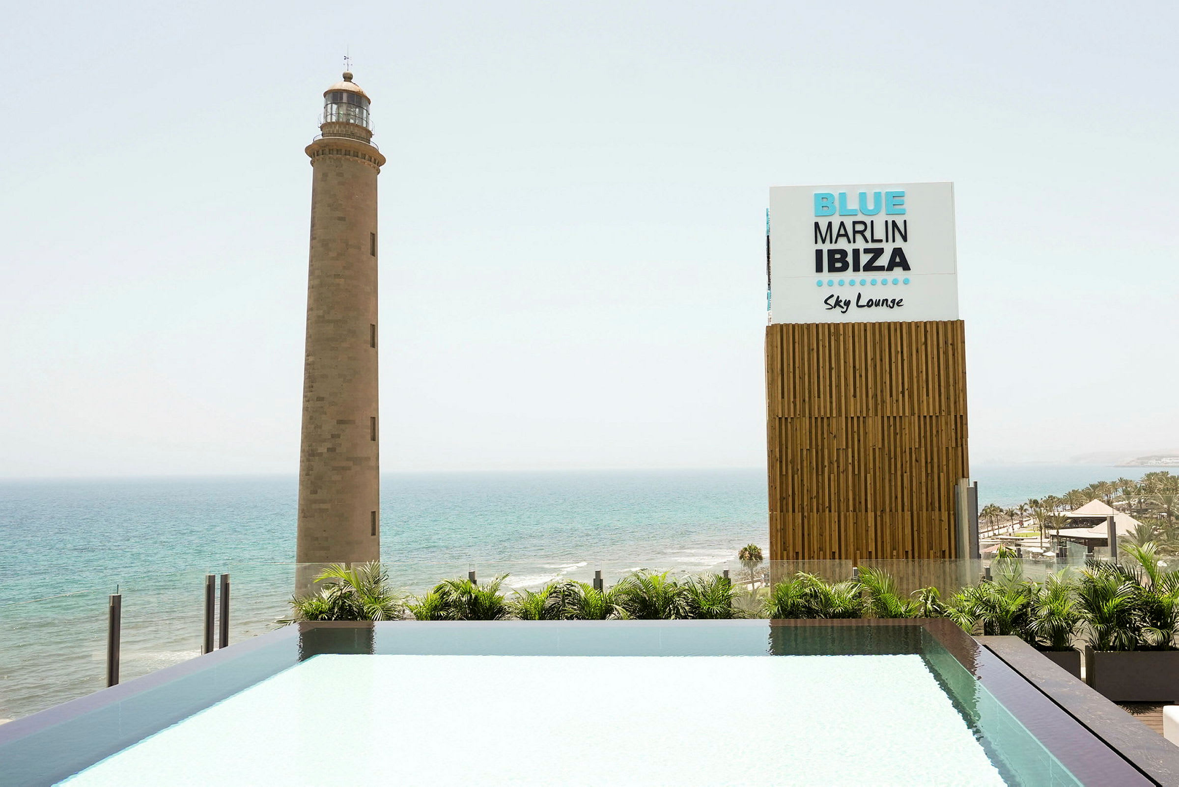 Et fyr ved havet ved siden af et skilt, der siger 'Blue Marlin Ibiza Sky Lounge'. (AI-genereret tekst)
