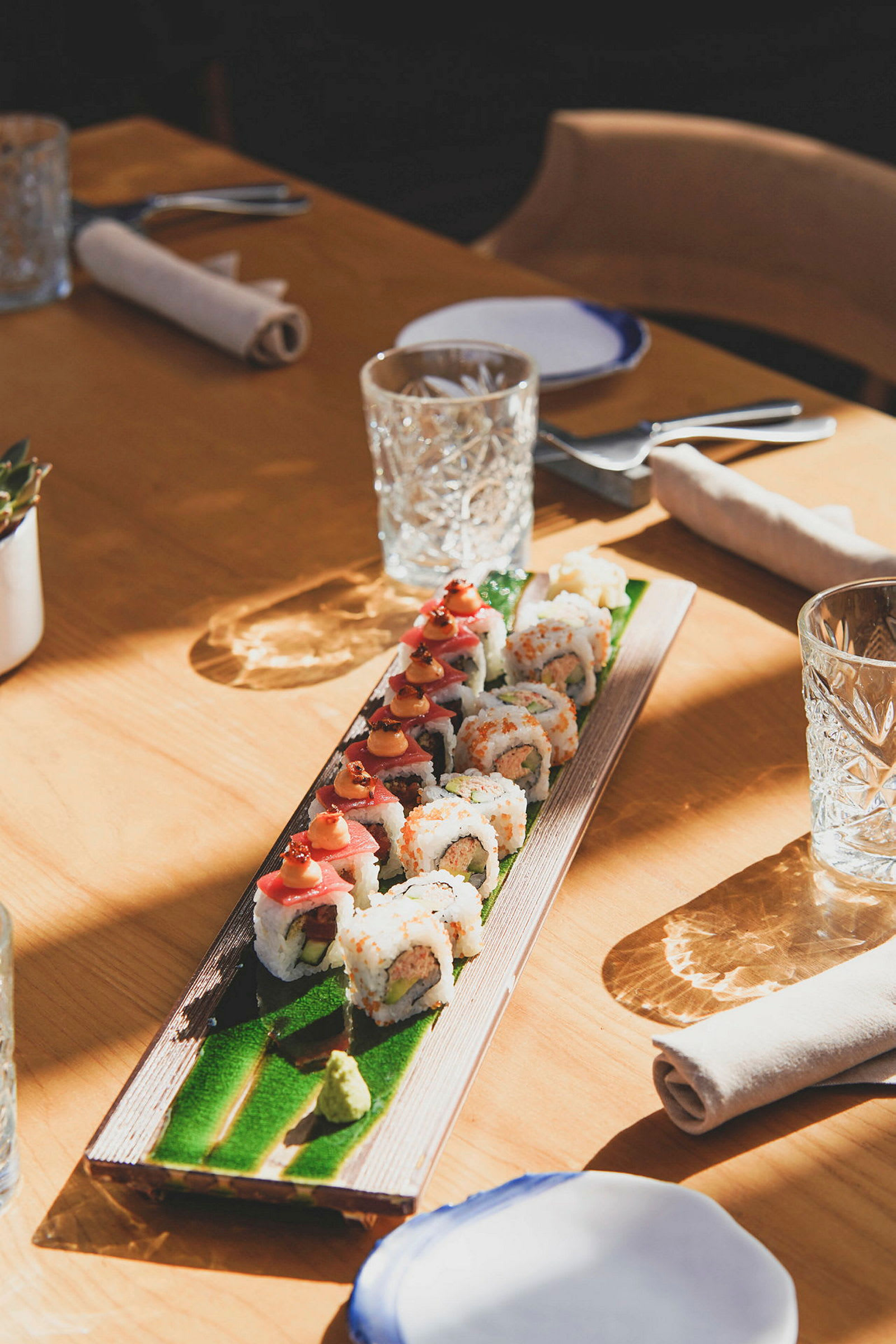 Sushi anrettet på et aflange fad på et bord dækket til måltid. (AI-genereret tekst)