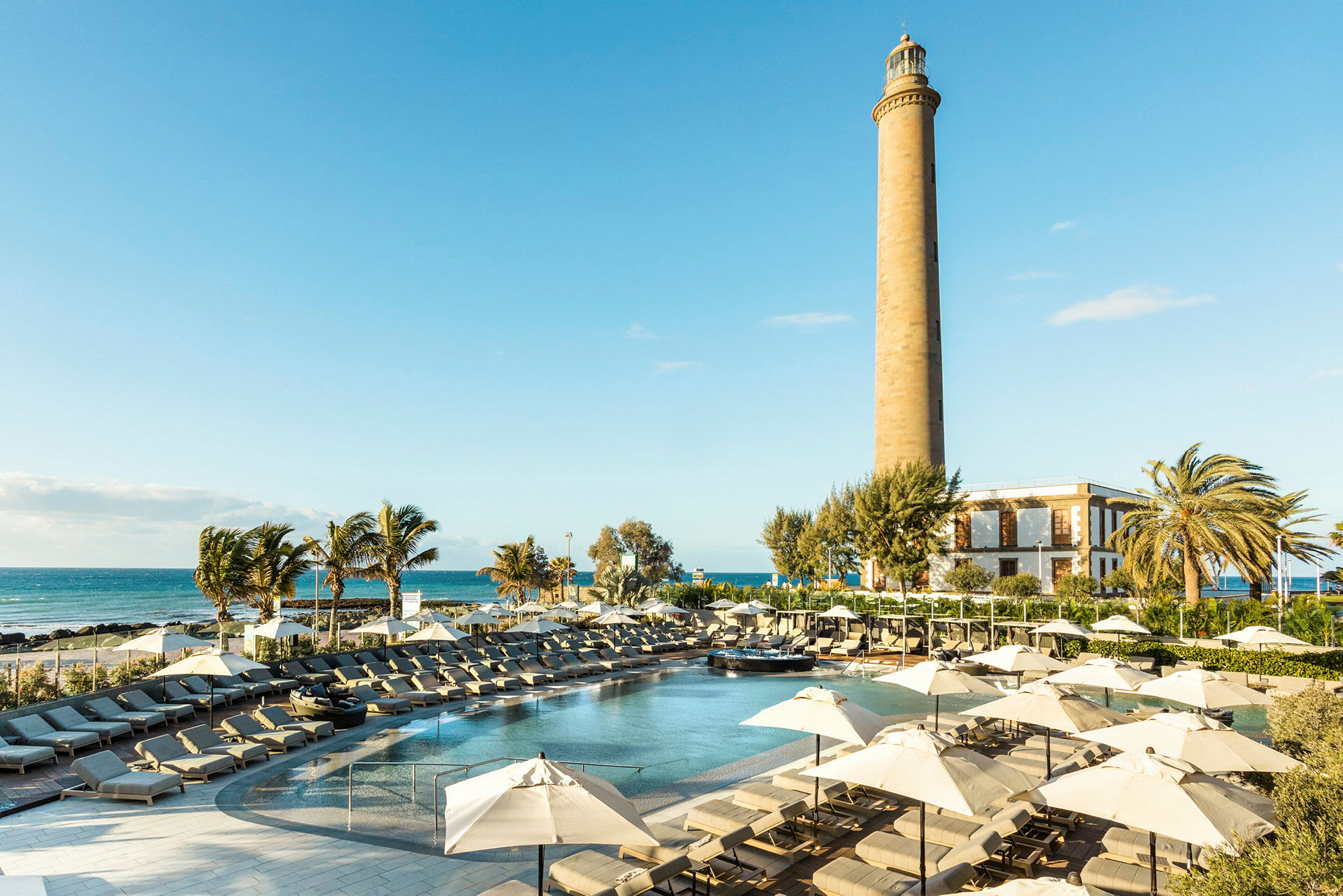 En solrig resort med pool, liggestole og parasoller samt et fyrtårn i baggrunden. (AI-genereret tekst)