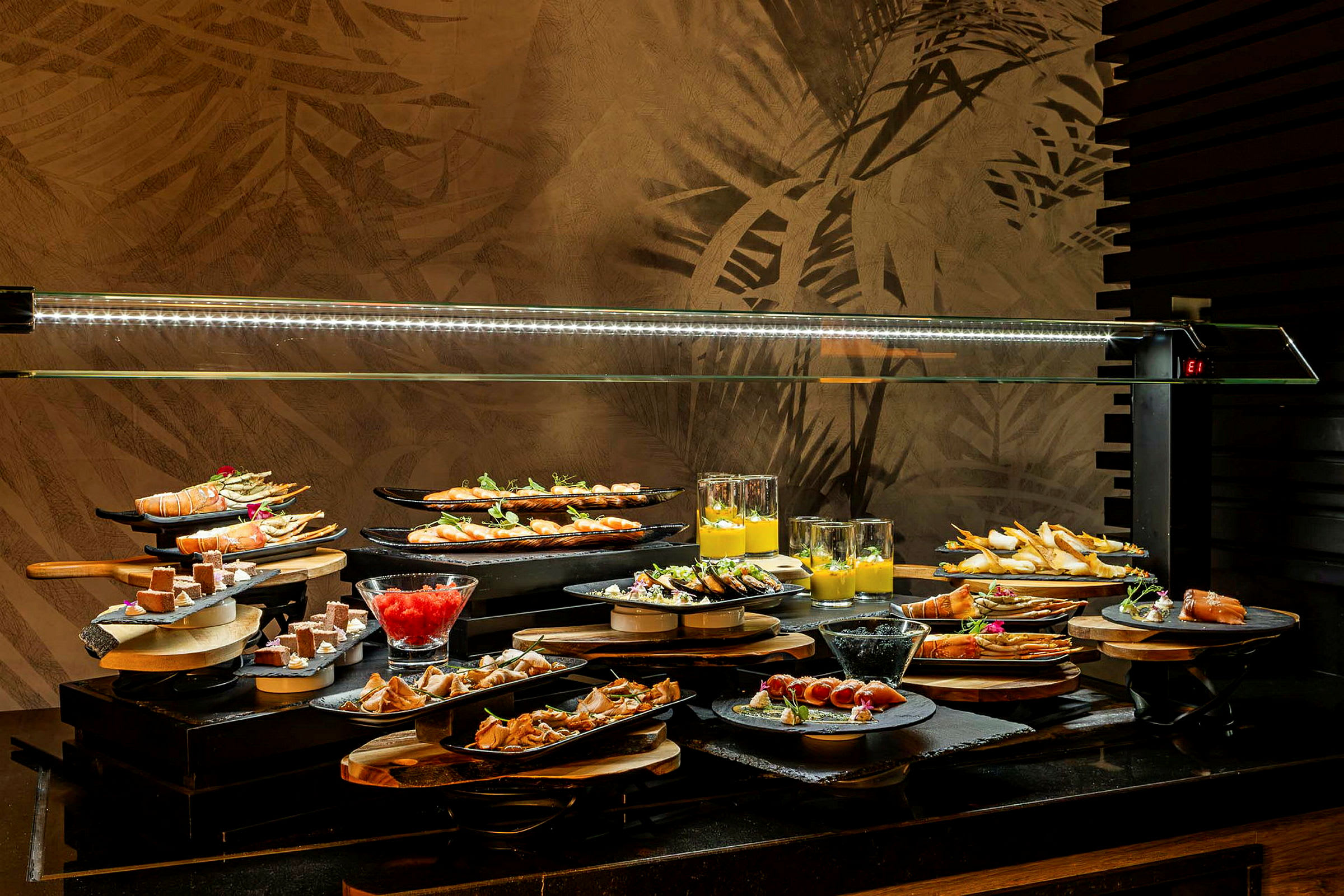 Et buffetbord med forskellige retter og desserter anrettet på tallerkener og i glas, under en glaskuppel. (AI-genereret tekst)