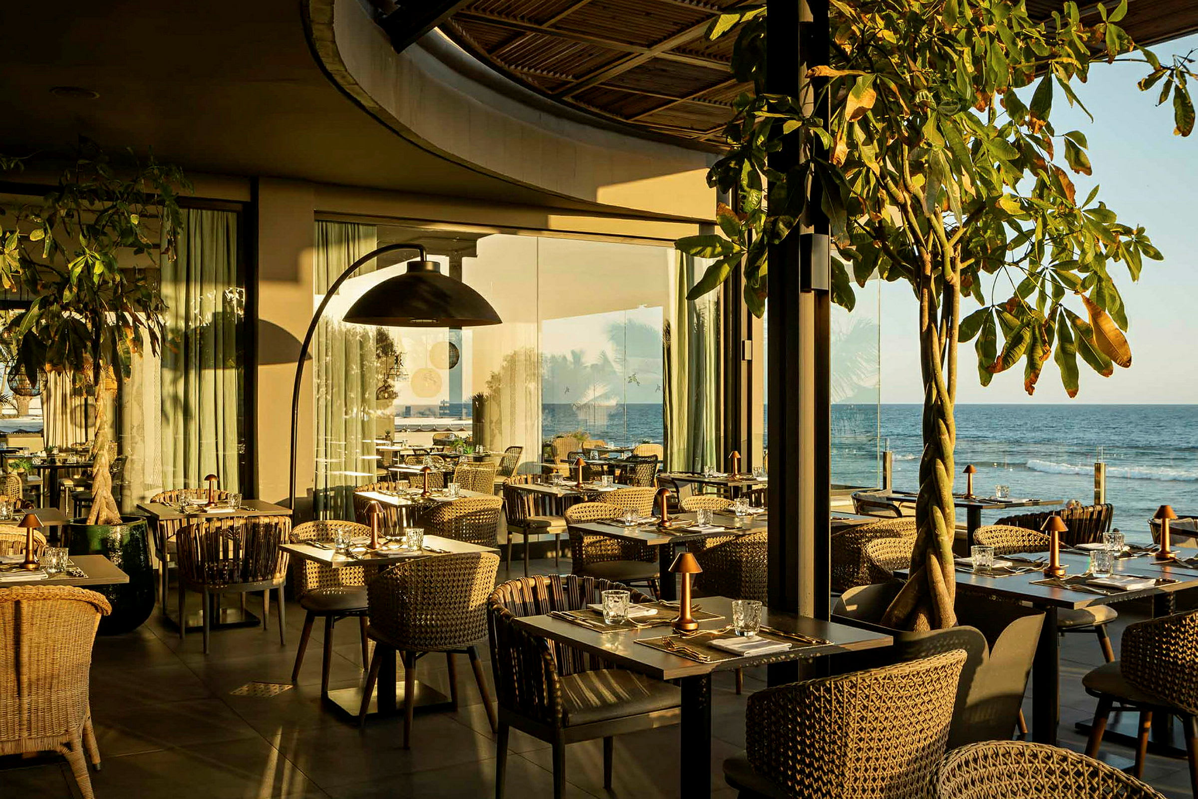 En restaurant med borde og stole tæt på havet, badet i sollys. (AI-genereret tekst)