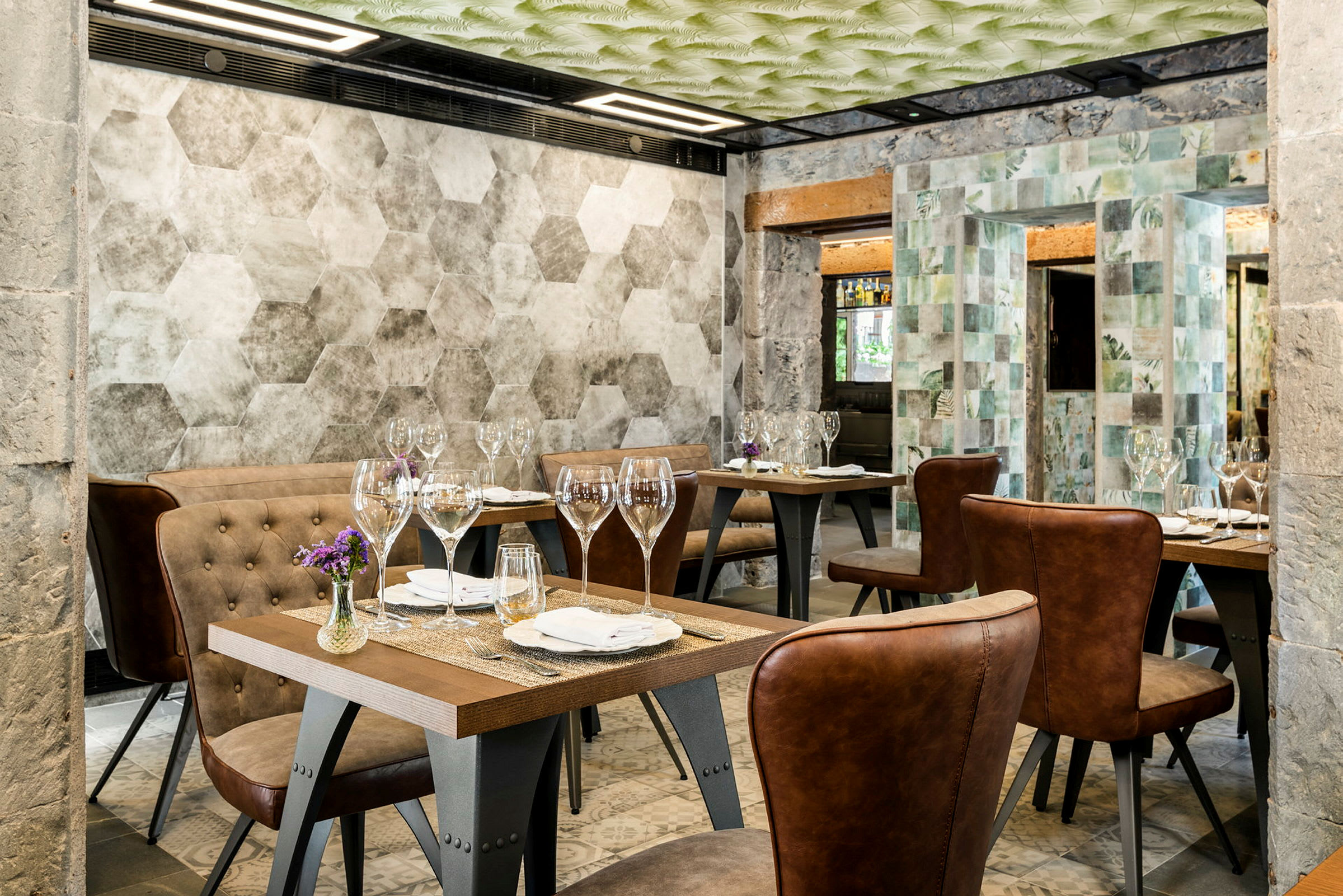 En restaurant med flere borde, dækket med glas og servietter. Stolene har brunt læder, og væggene har geometriske mønstre. (AI-genereret tekst)