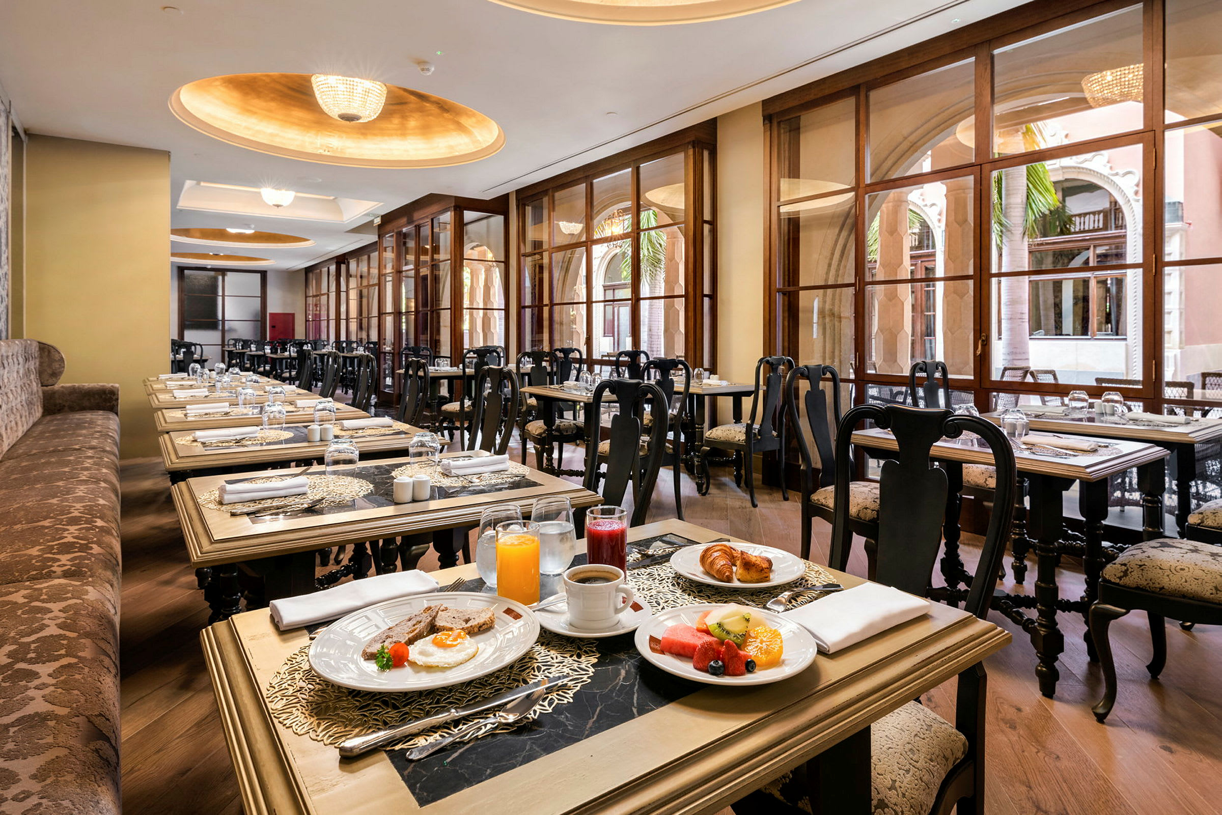 Billede af en restaurant med elegante siddeområder og vinduer samt borde dækket med morgenmad. (AI-genereret tekst)