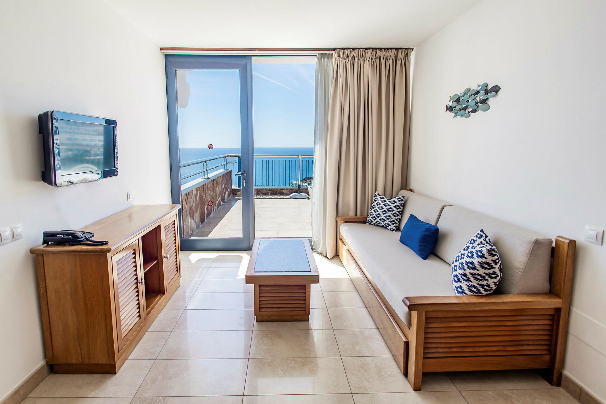 Et hotelværelse med siddeområde og udsigt til havet fra en balkon. (AI-genereret tekst)