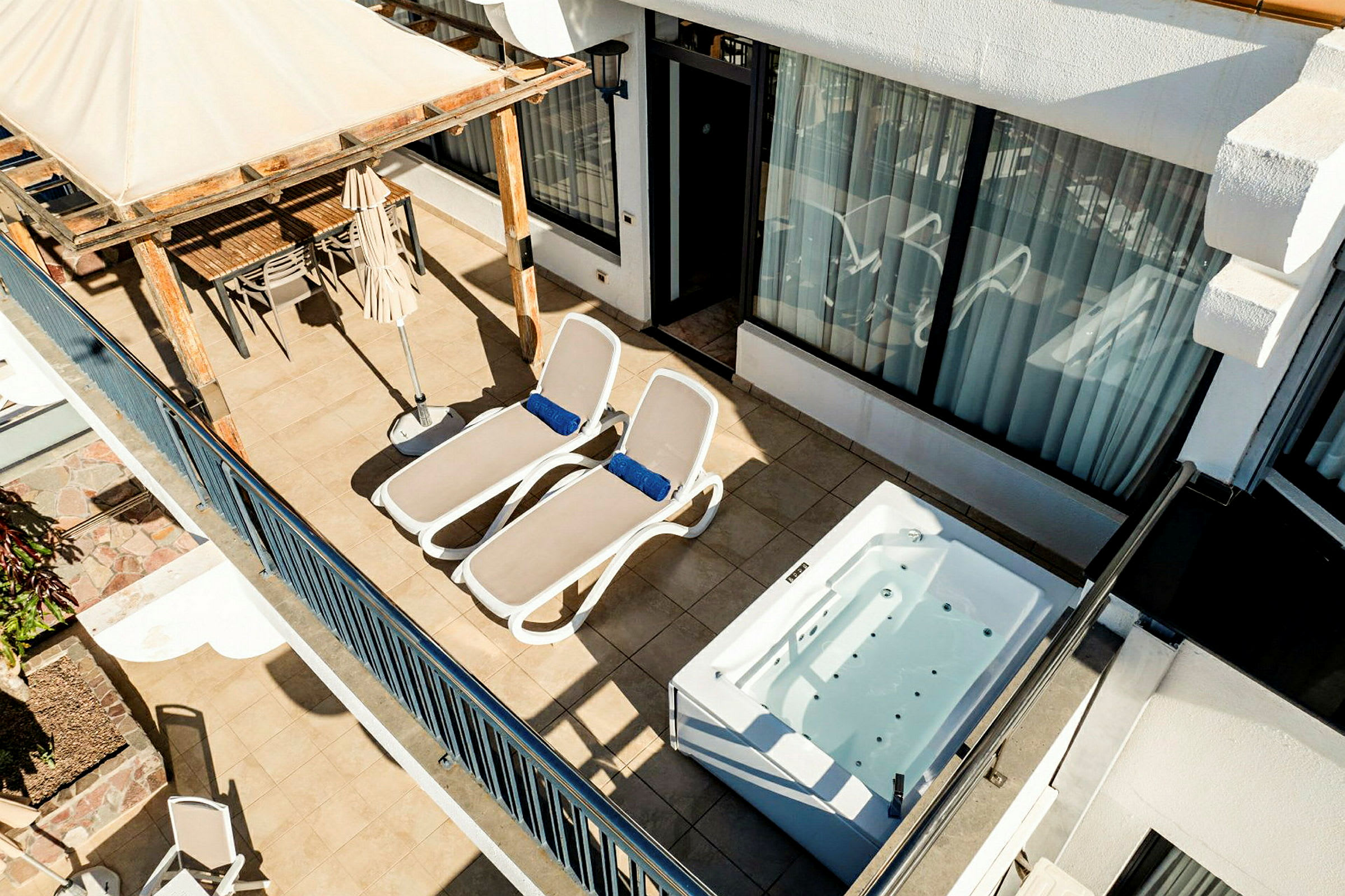 En terrasse med to liggestole, et spabad og en spiseplads under en pergola. (AI-genereret tekst)