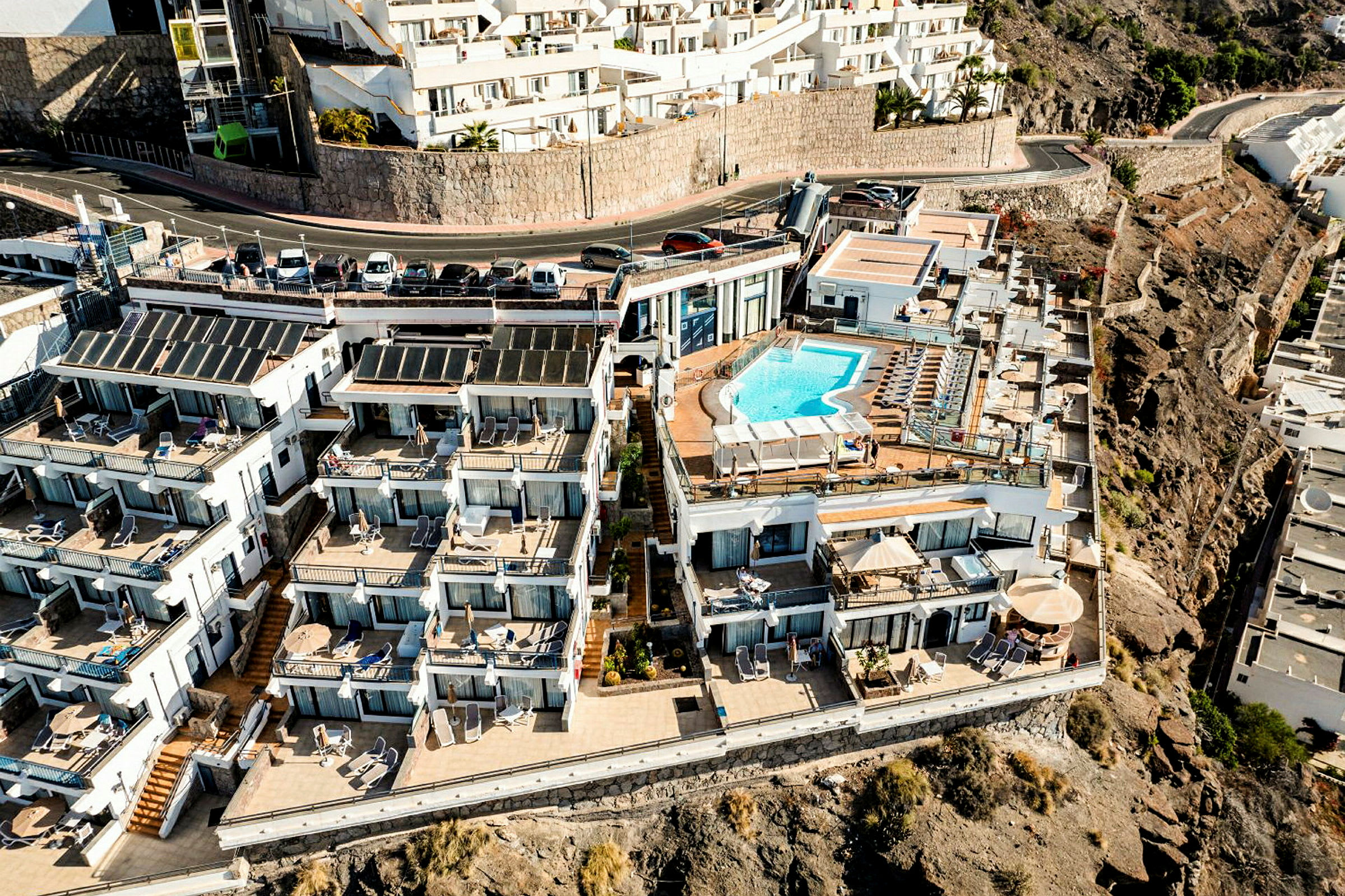 Hotelkompleks med lejligheder og en udendørs pool på en klippeafsats. (AI-genereret tekst)