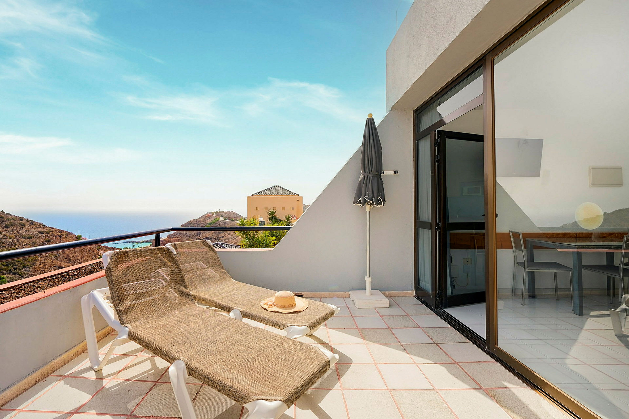 Terrasse med liggestole og parasol, havudsigt i baggrunden. (AI-genereret tekst)