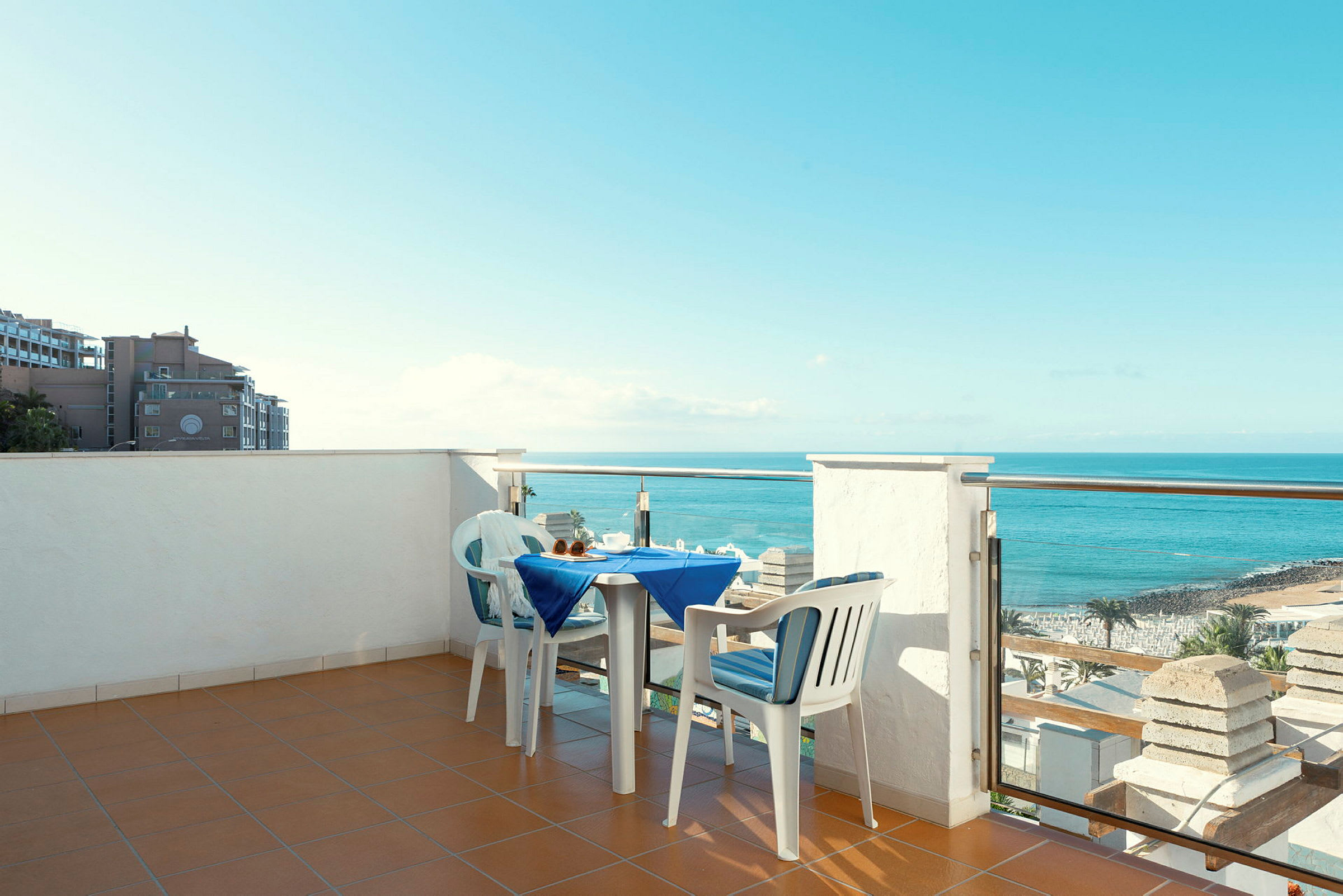En terrasse med et dækket bord og to stole, med udsigt over havet og stranden. (AI-genereret tekst)