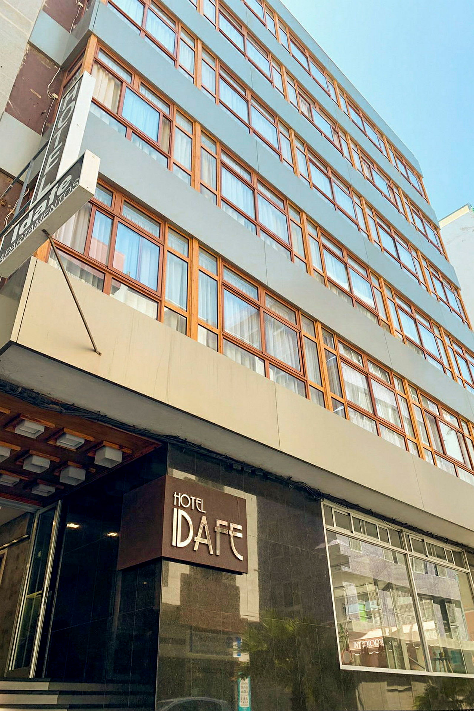 En bygning med flere etager og skilt med teksten 'Hotel Idafe' ved indgangen. (AI-genereret tekst)