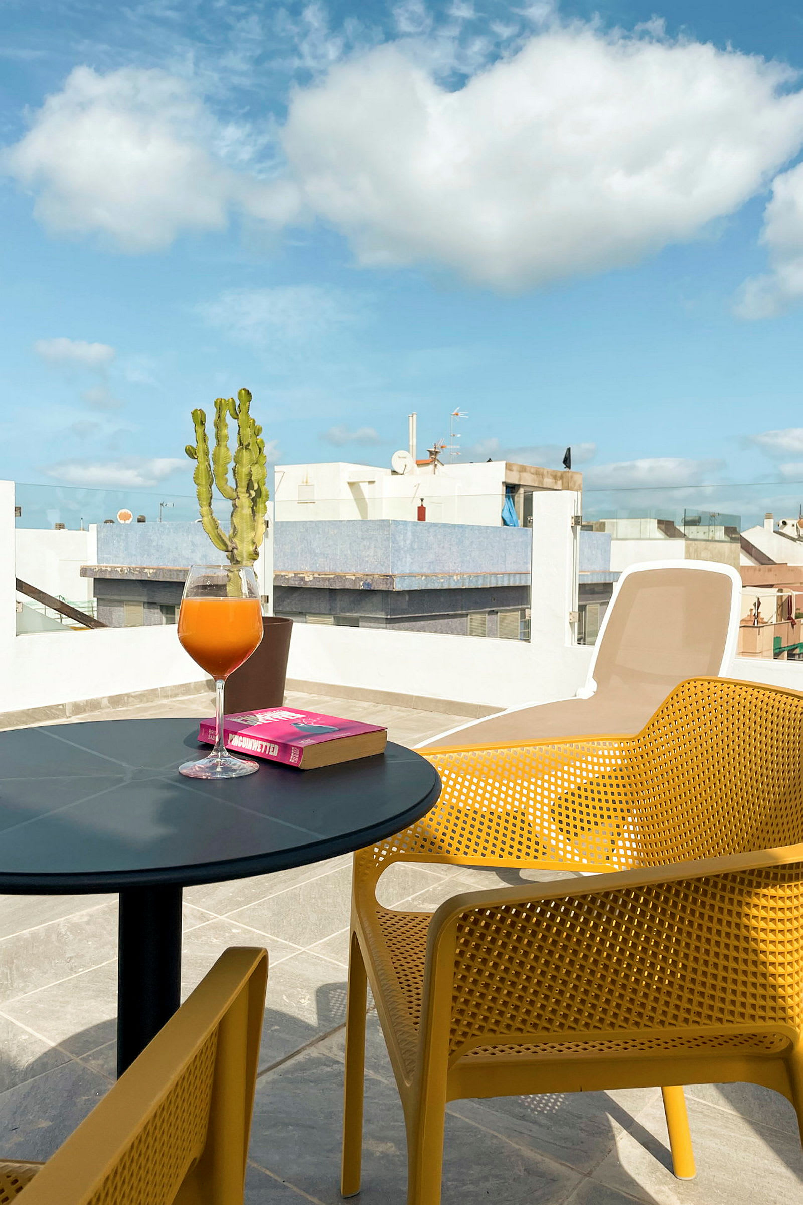 En terrasse med et bord, en bog og et glas juice. (AI-genereret tekst)