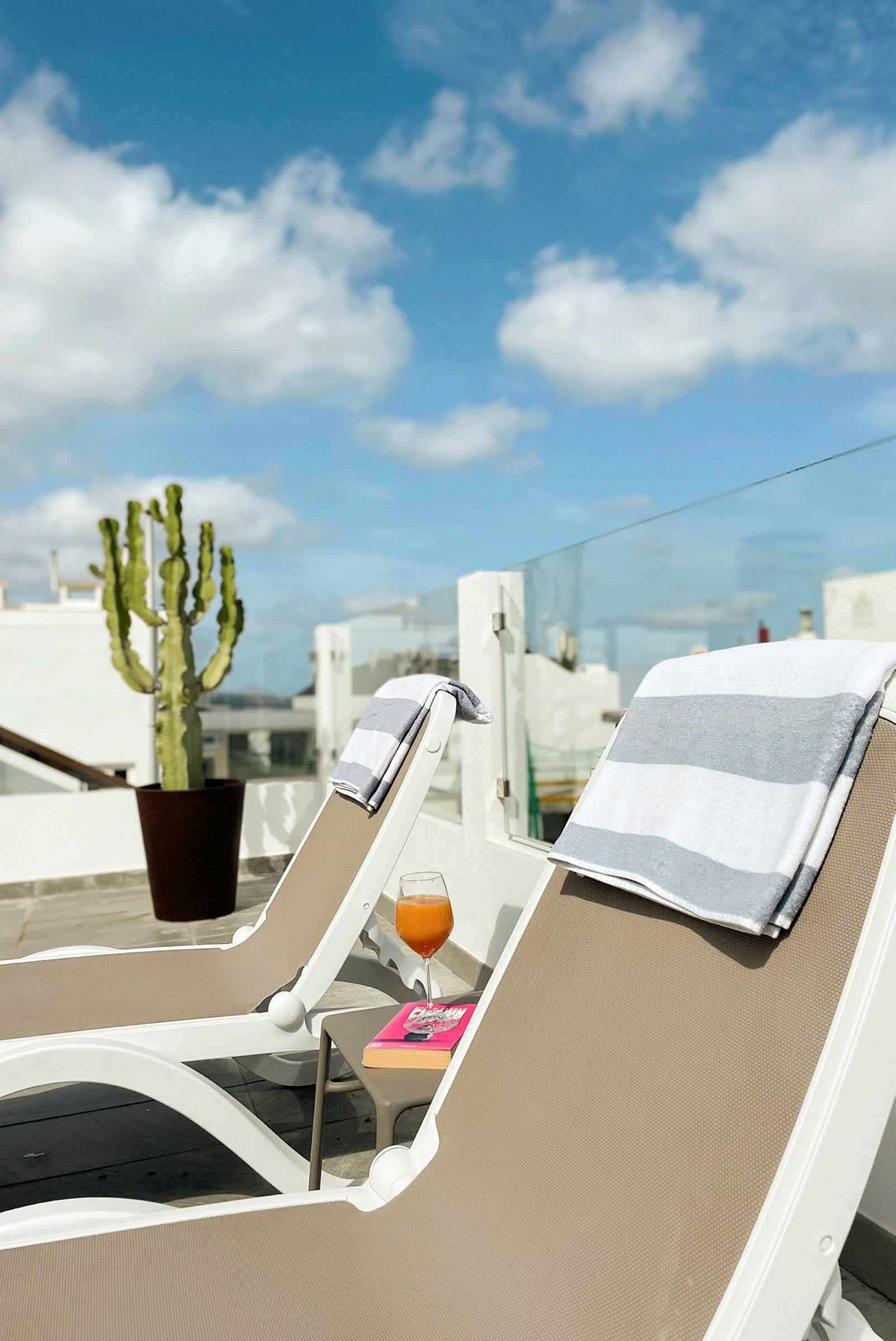 To liggestole med håndklæder på en terrasse, en drink og en bog på et bord ved siden af. (AI-genereret tekst)