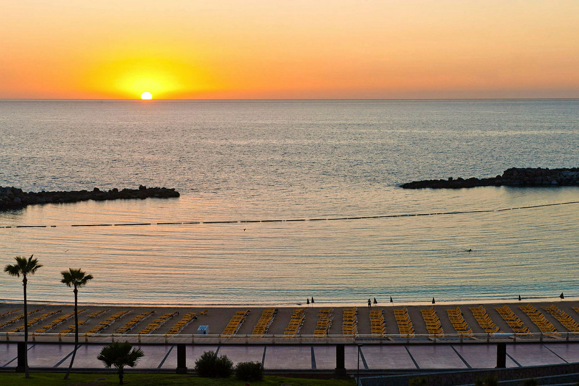Solnedgang over en strand med liggestole og havet. (AI-genereret tekst)