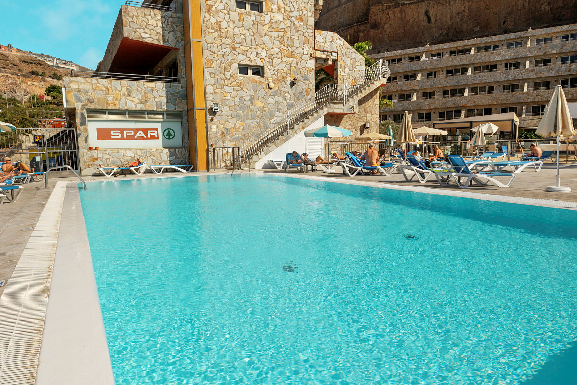 Udendørs pool ved hotel med liggestole og parasoller. (AI-genereret tekst)