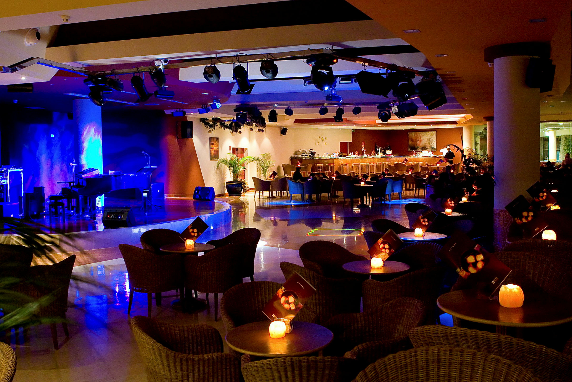 Interiør af en oplyst bar og scene med siddepladser omkring små borde. (AI-genereret tekst)