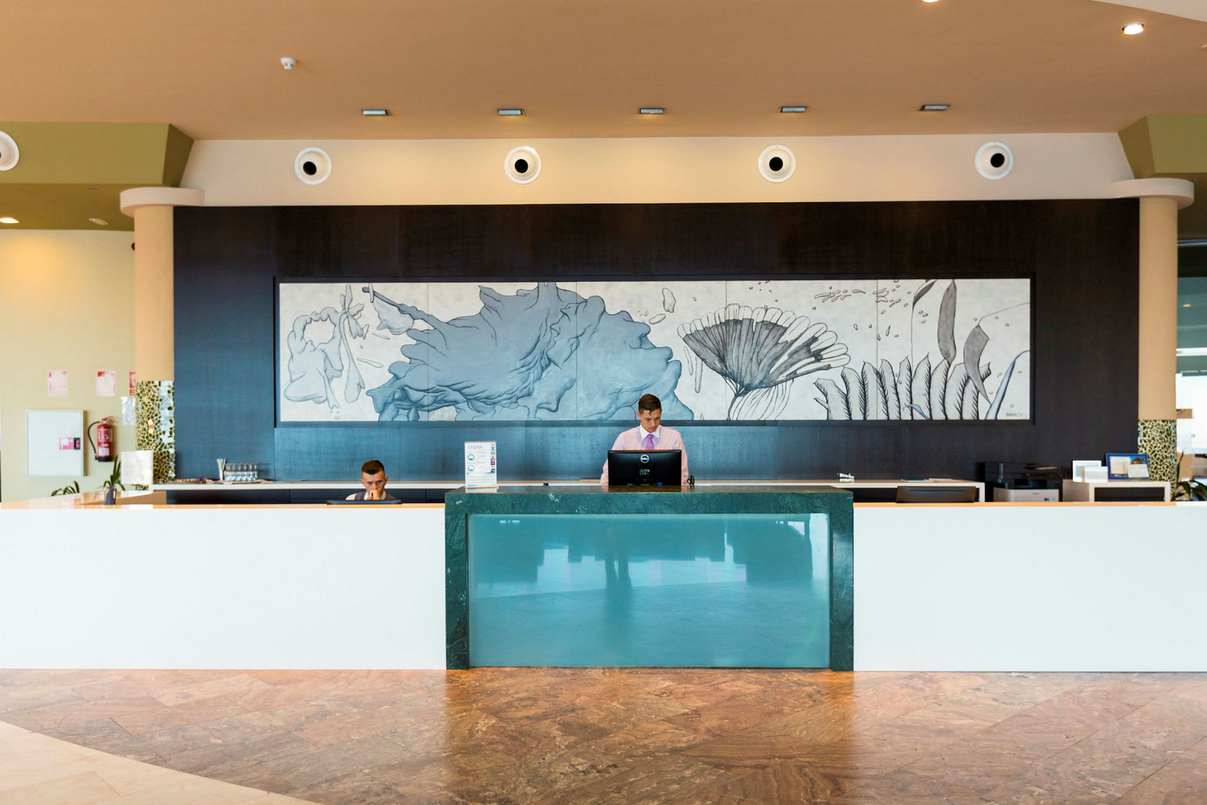 Hotellets reception med moderne indretning og et dekorativt vægmaleri. (AI-genereret tekst)