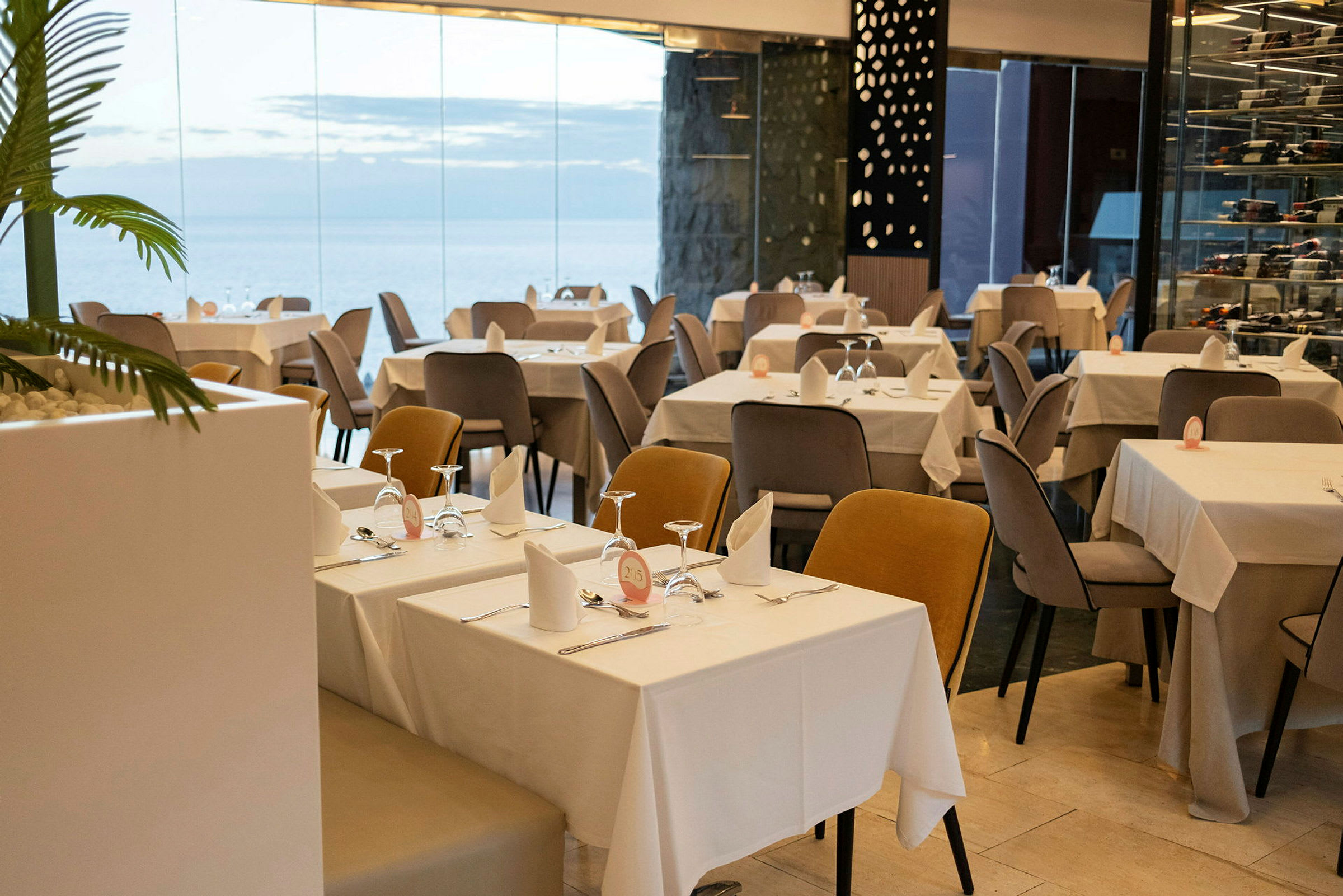 Restaurant med dækkede borde og stole i et moderne miljø med glasvægge. (AI-genereret tekst)