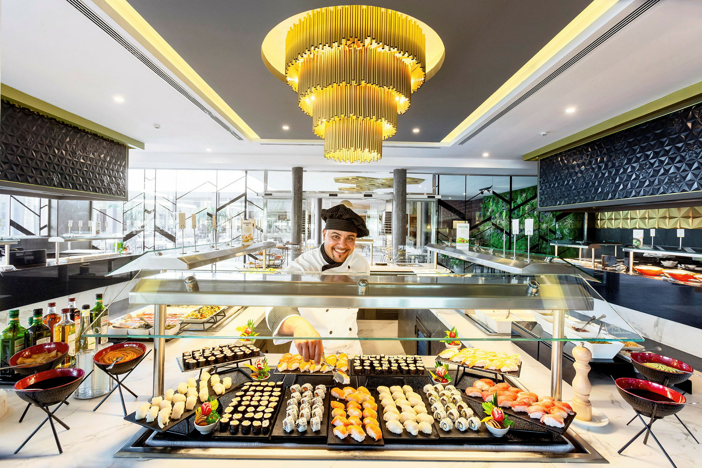 En elegant madservering med sushi og andre småretter på en buffet, oplyst af en luksuriøs lysekrone. (AI-genereret tekst)