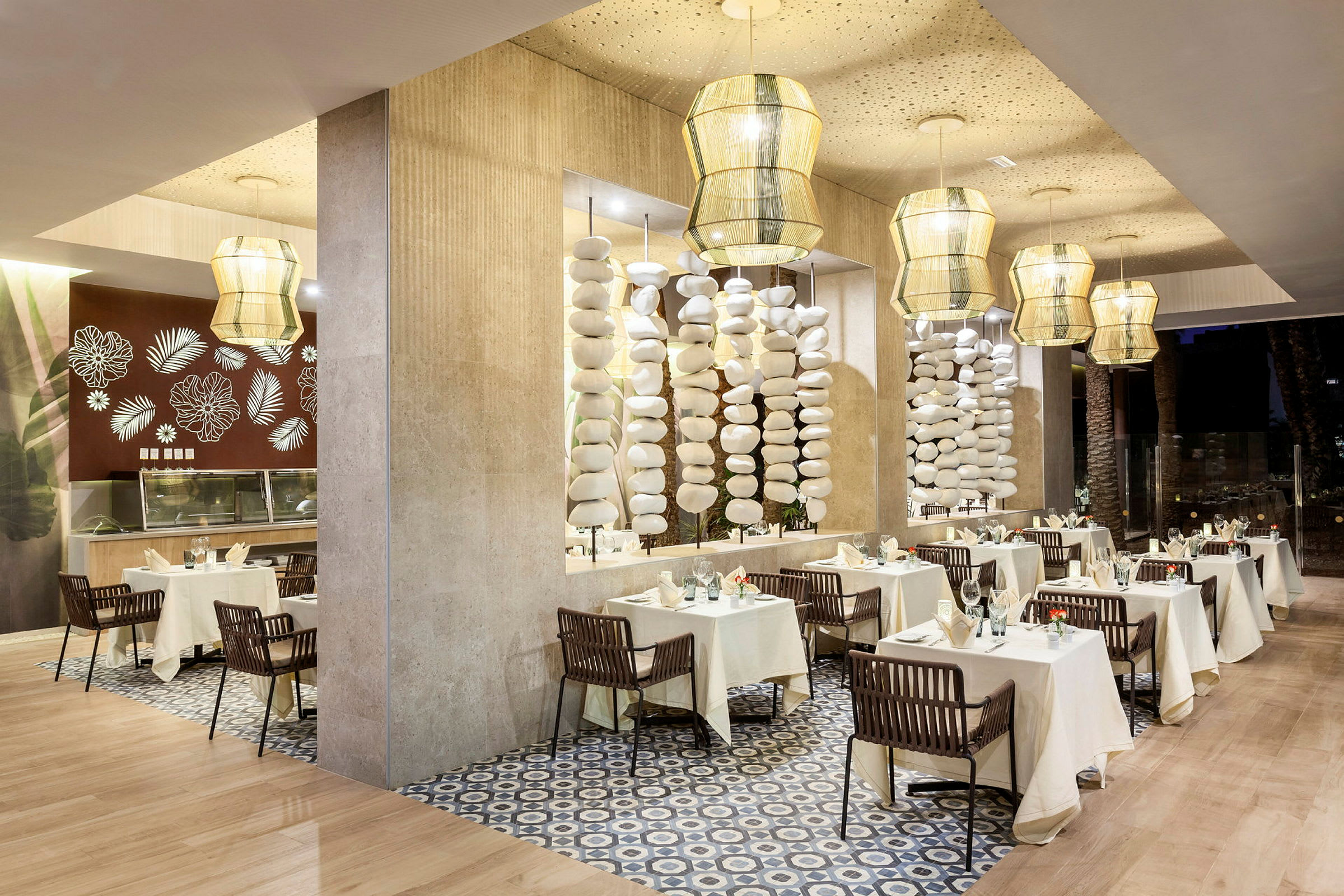 En elegant restaurantinteriør med borde dækket med hvide duge og stilfuldt dekoreret med porcelæn og glas. Lyse hængende lamper og dekorative søjler fuldender designet. (AI-genereret tekst)