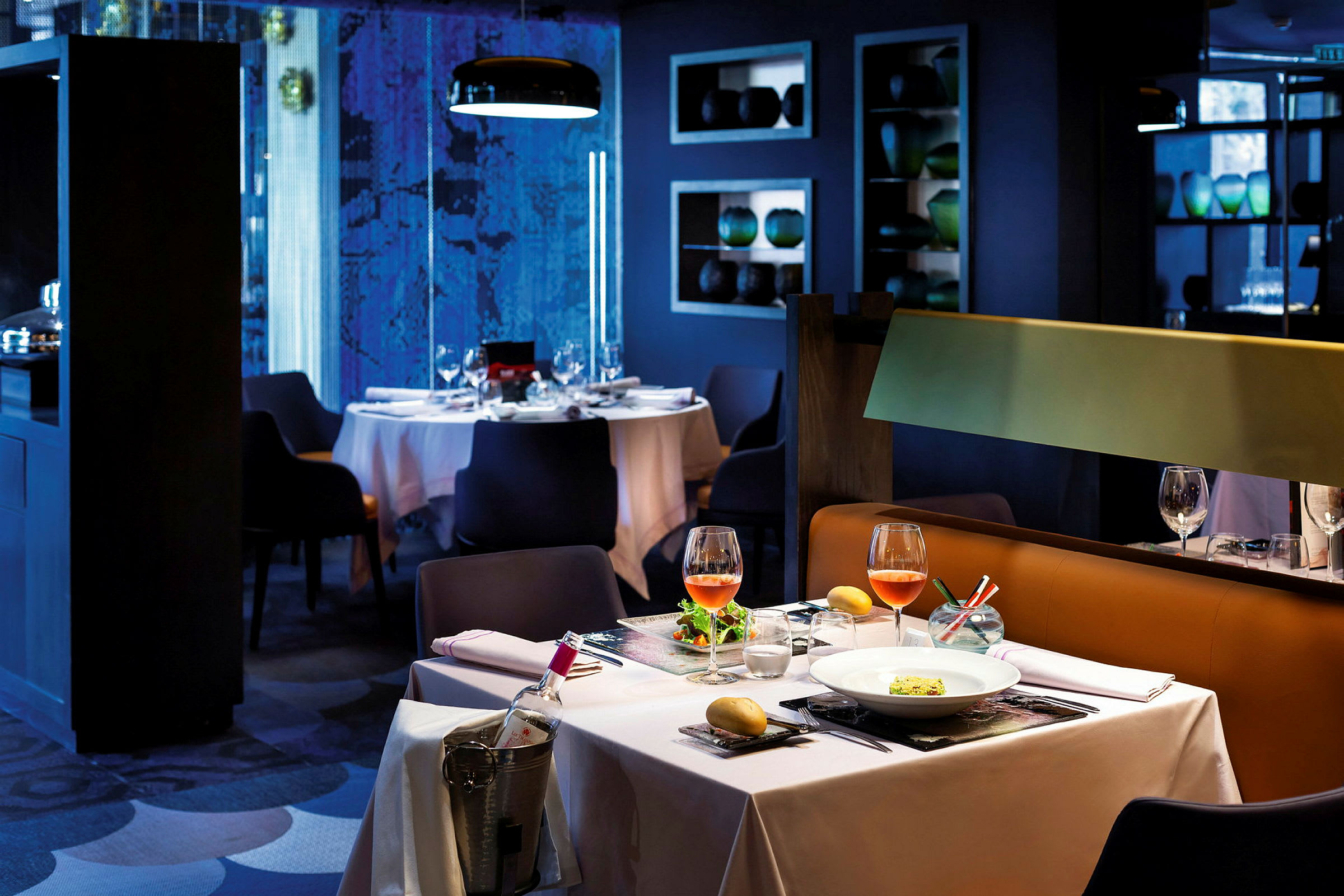 Et elegant restaurationsbord med hvid dug, to vinglas og en anrettet ret. En vinflaske står i is ved siden. (AI-genereret tekst)