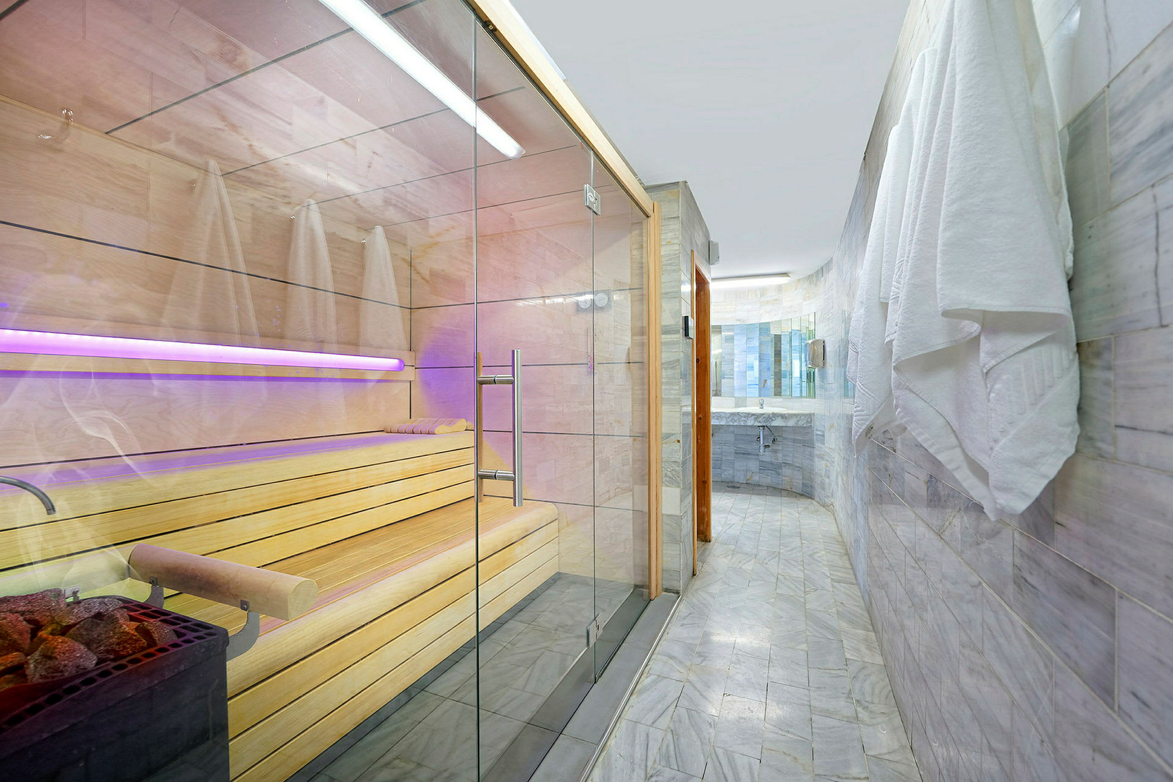 Billedet viser en moderne sauna med glasdøre og træinteriør samt et badeværelse med flisbelagte vægge og håndklæder hængende på siden. (AI-genereret tekst)