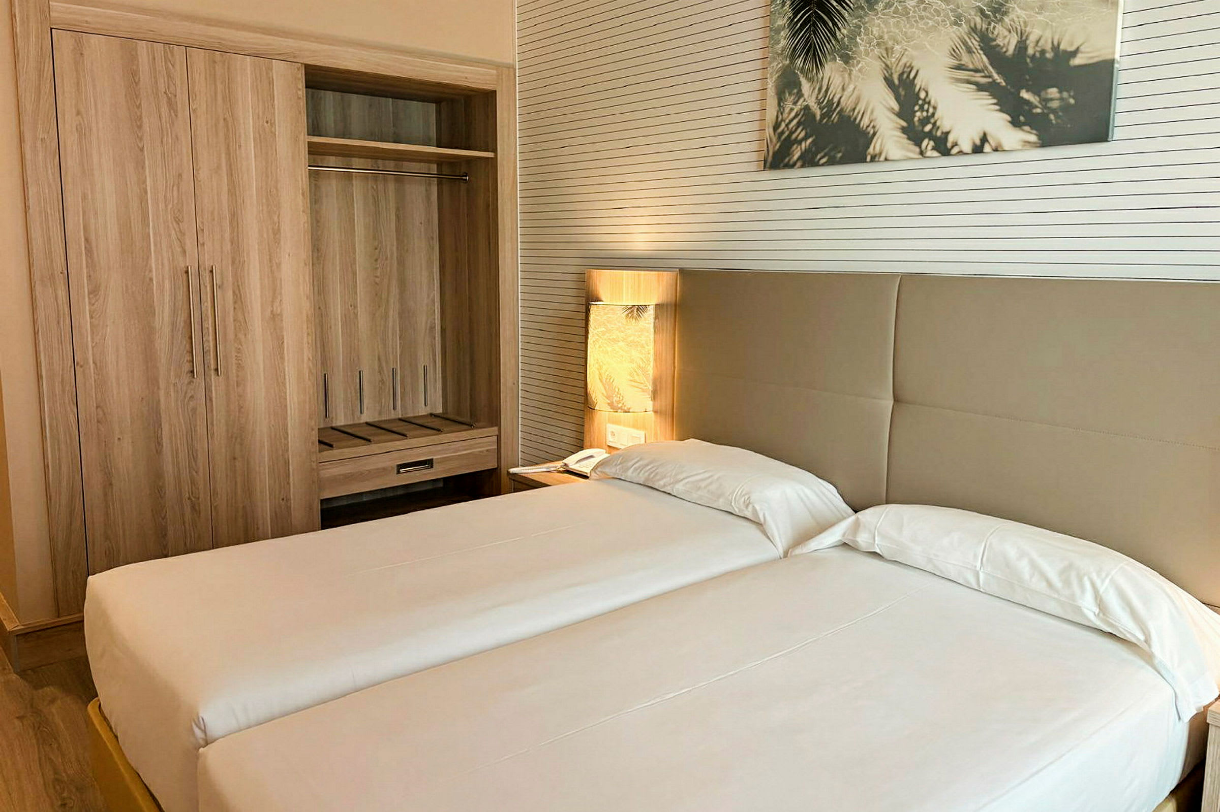Hotelværelse med to enkeltsenge, et garderobeskab og en bordlampe ved siden af sengen. (AI-genereret tekst)