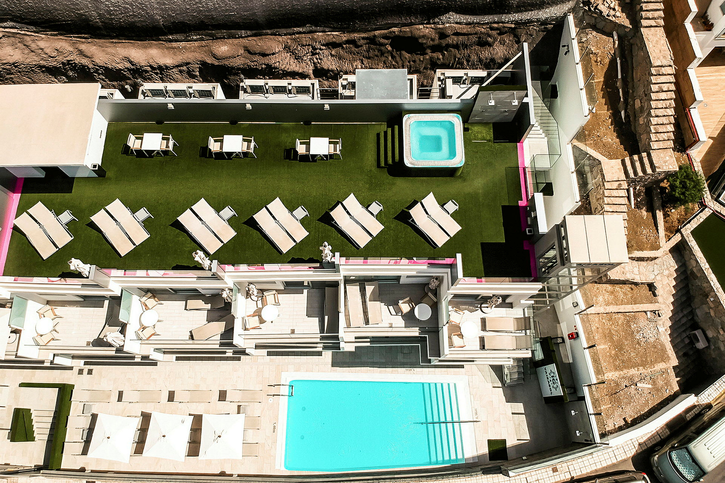 Udsigt fra oven over hotelområde med frodig græsplæne, liggestole, boblebad og swimmingpool. (AI-genereret tekst)