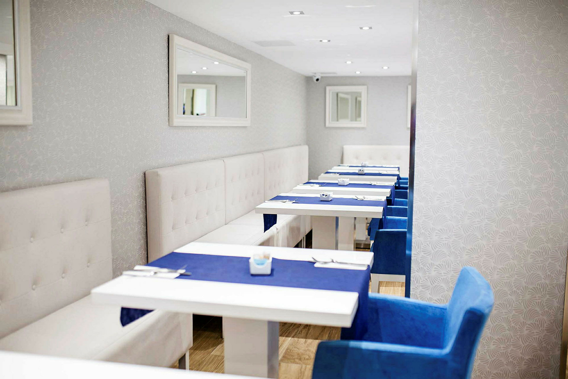 En restaurant med hvide borde, blå stole og hvide vægge med et spejl. (AI-genereret tekst)