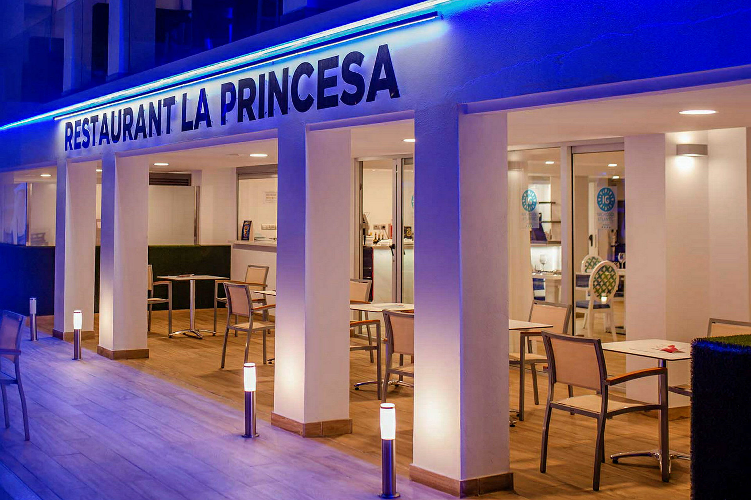 Restaurant La Princesa med borde og stole på en oplyst terrasse. (AI-genereret tekst)