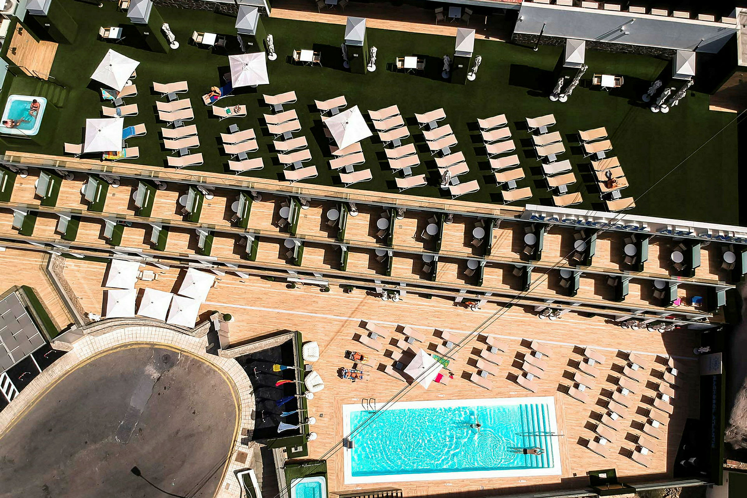 Luftfoto af hotelområde med pool, liggestole og parasoller. (AI-genereret tekst)
