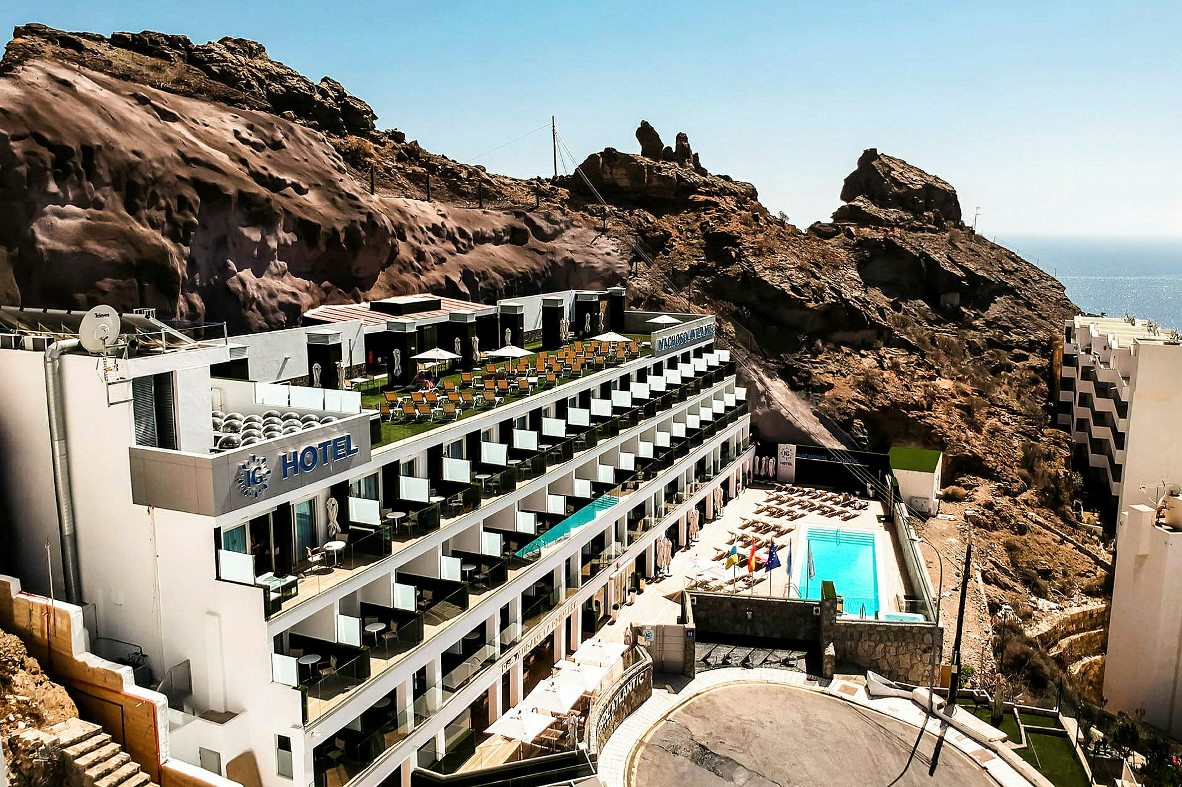 Et hotel beliggende ved en bjergskråning med poolområde og havudsigt. (AI-genereret tekst)