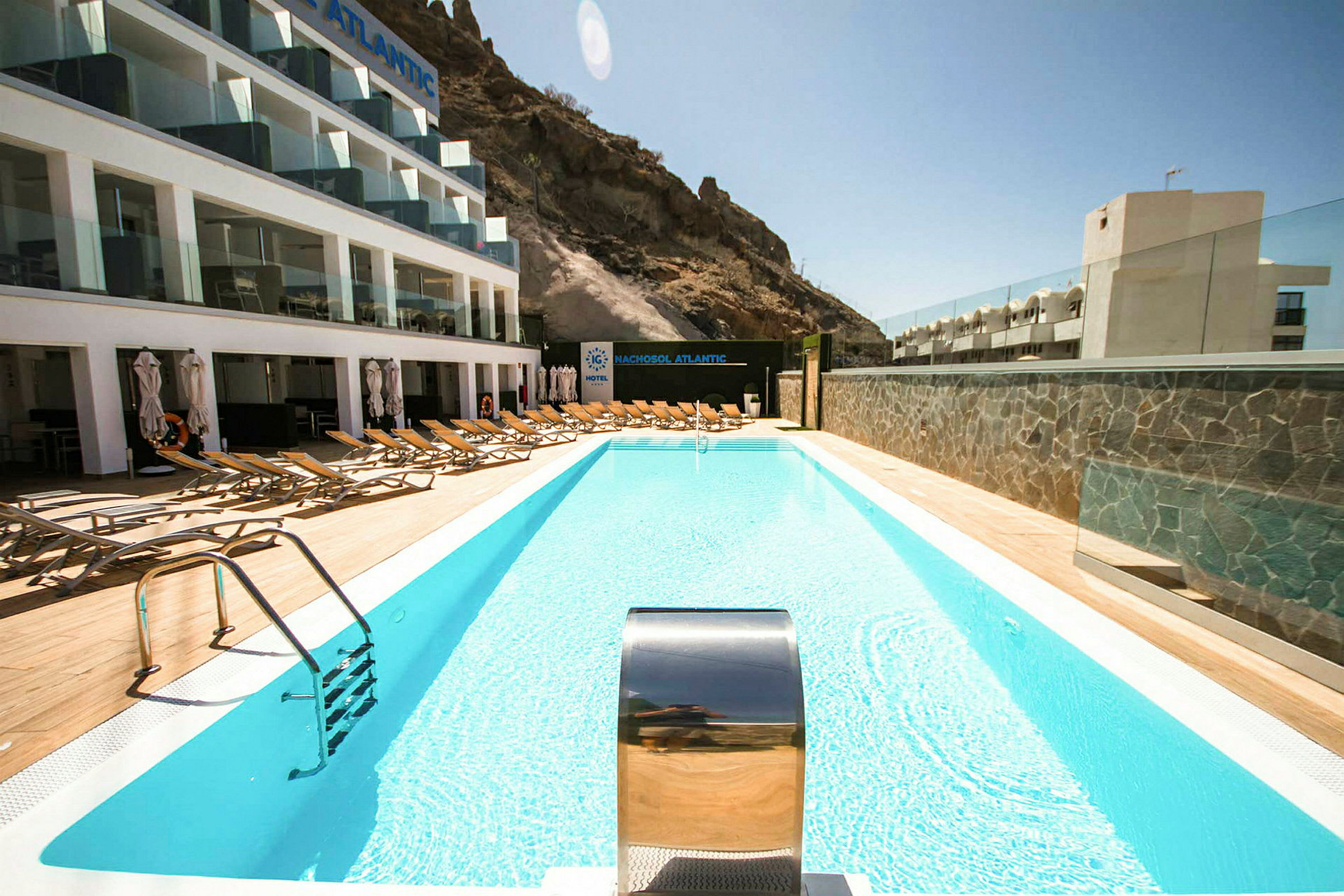 Udendørs swimmingpool med liggestole og hotelbygning i baggrunden. (AI-genereret tekst)