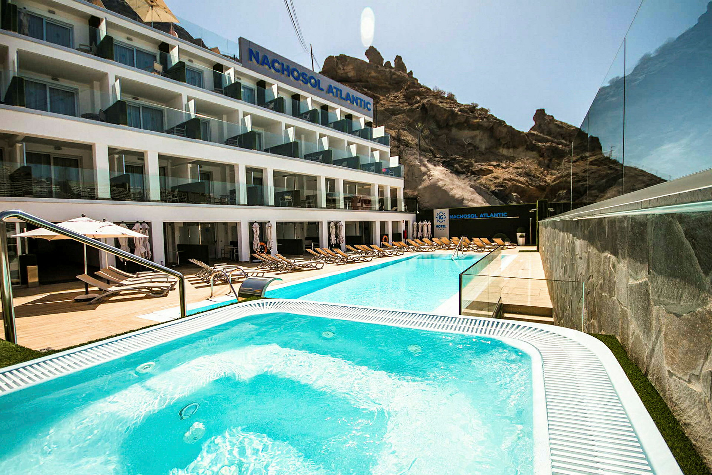 Hotelfacade med pool og liggestole i forgrunden. (AI-genereret tekst)