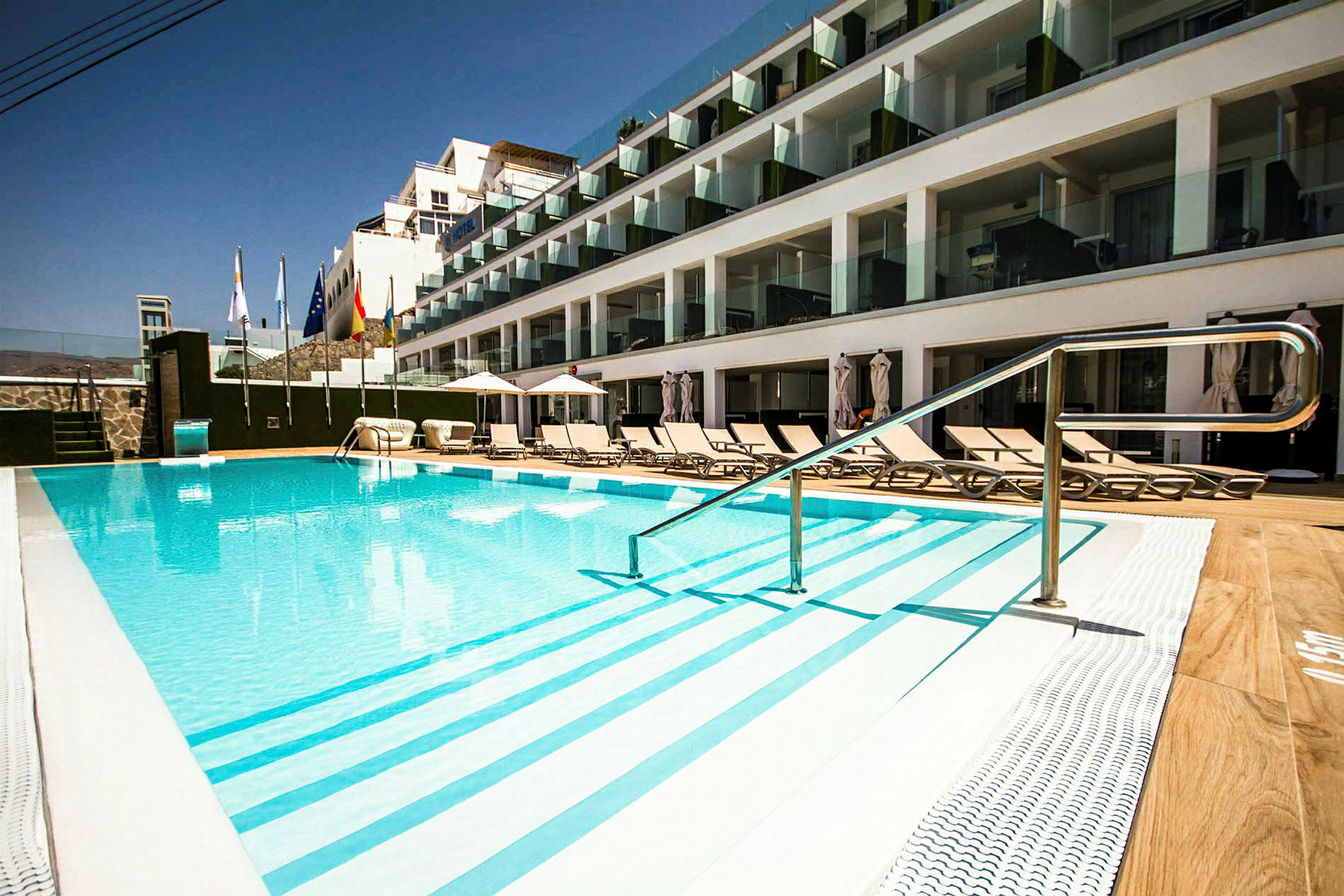 Udendørs pool ved hotel med solsenge og glasaltaner. (AI-genereret tekst)