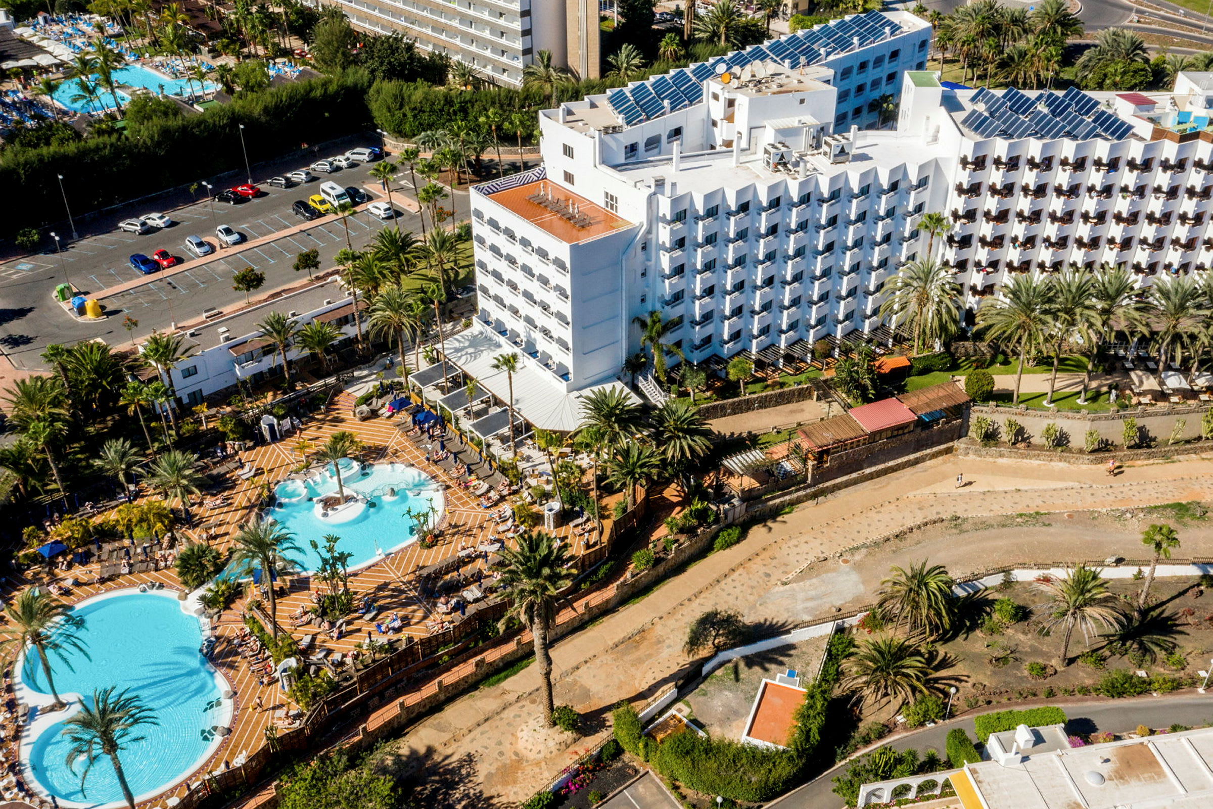Luftfoto af hotelområde med flere pools og omkringliggende grønne områder. (AI-genereret tekst)