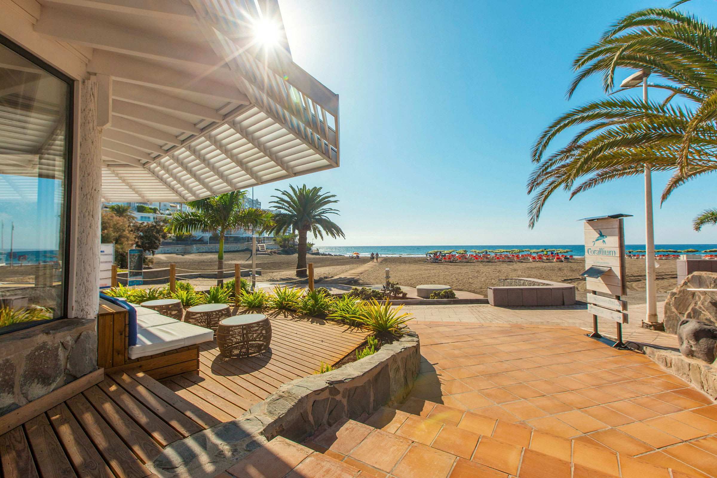 Udsigt over en solrig terrasse med strand og hav i baggrunden. (AI-genereret tekst)
