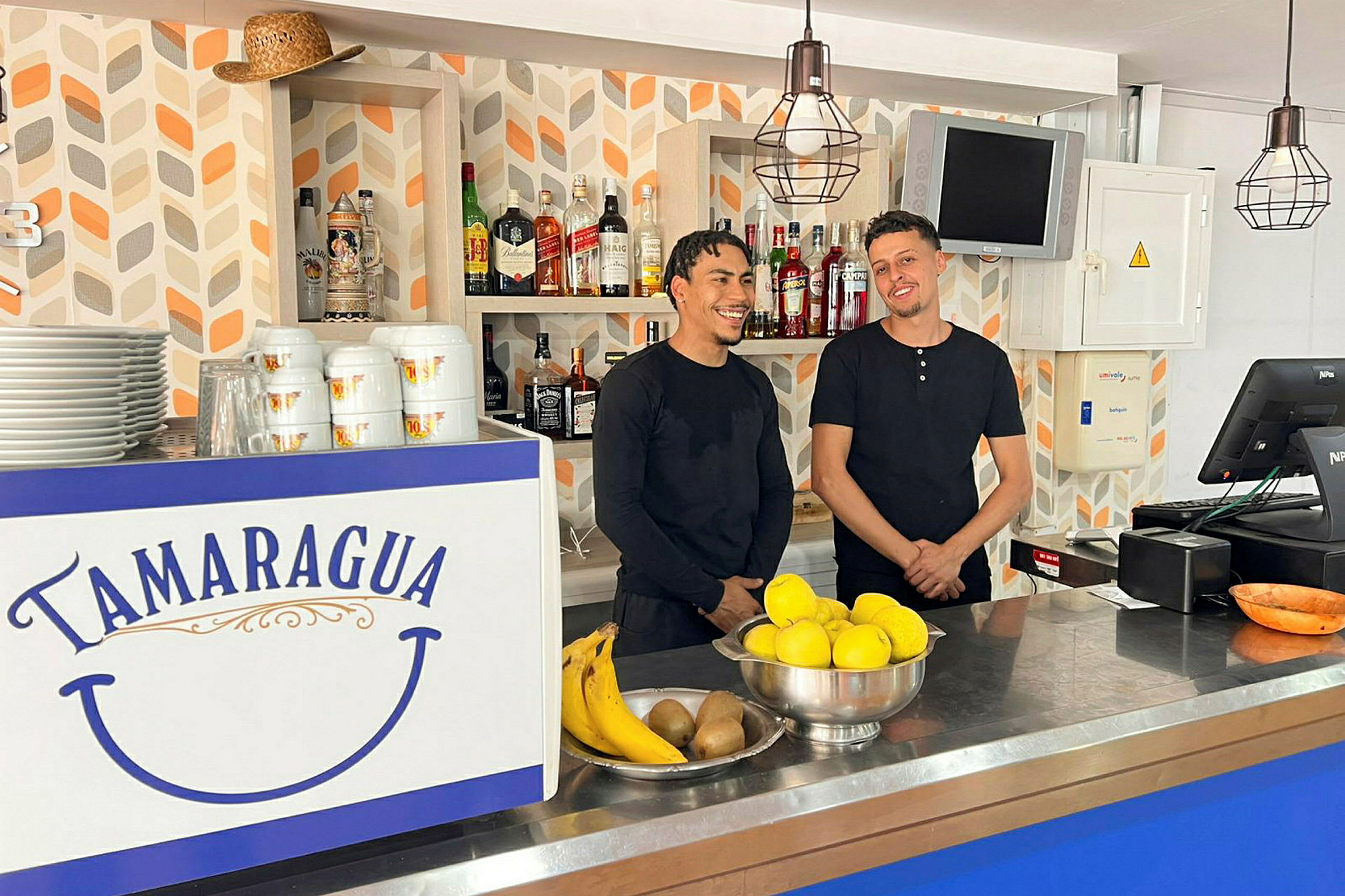 En bar med en disk dekoreret med teksten "Tamaragua". På disken er der frugt og porcelæn. Baggrunden har hylder med flasker. (AI-genereret tekst)