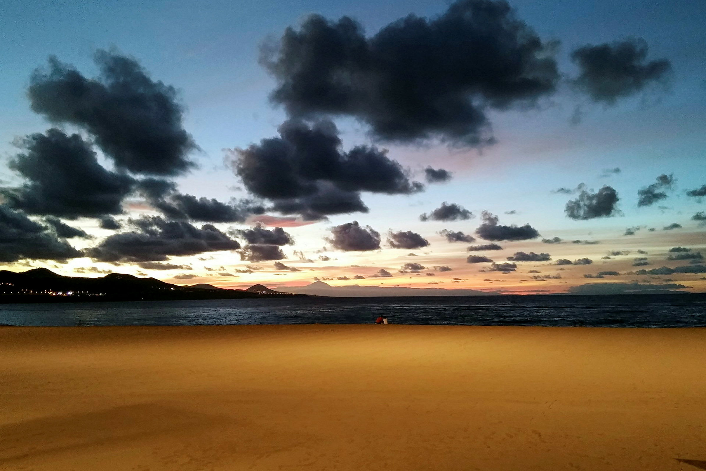Sandstrand ved havet under en aftenhimmel med skyer og solnedgang. (AI-genereret tekst)