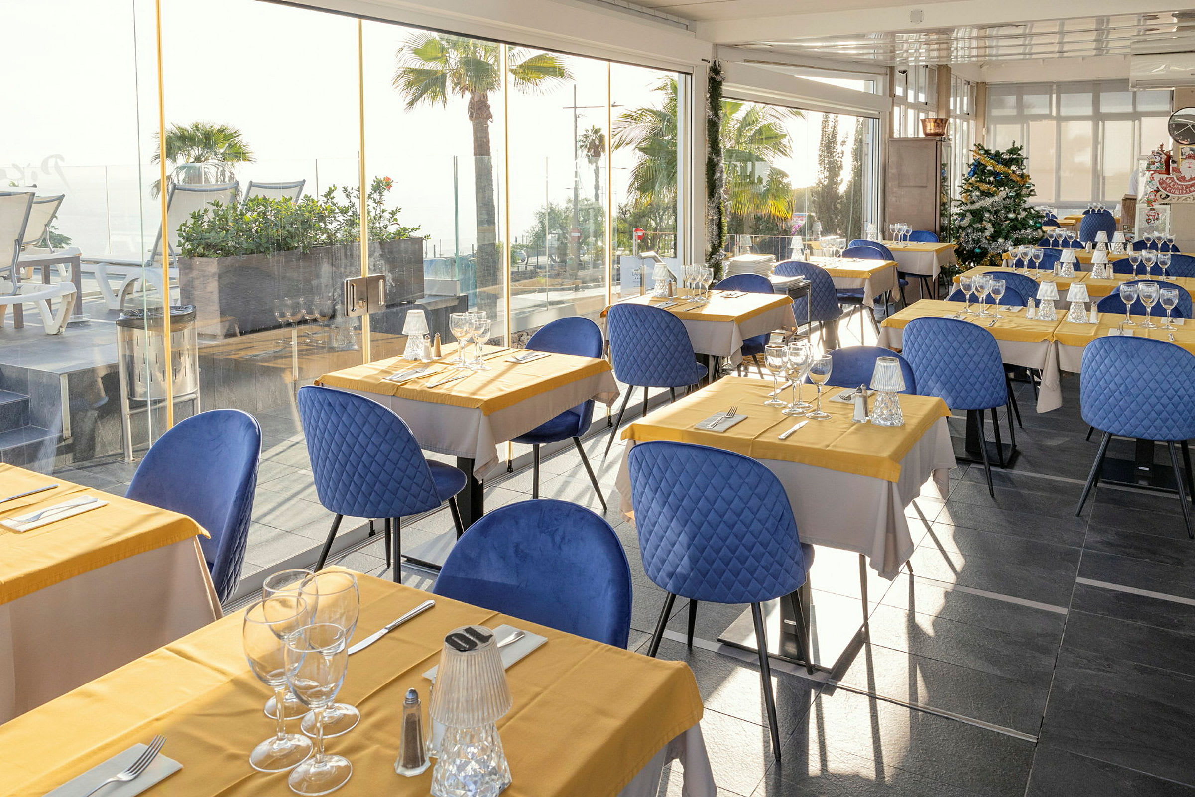 Restaurant med borde dækket med gule duge og blå stole. (AI-genereret tekst)