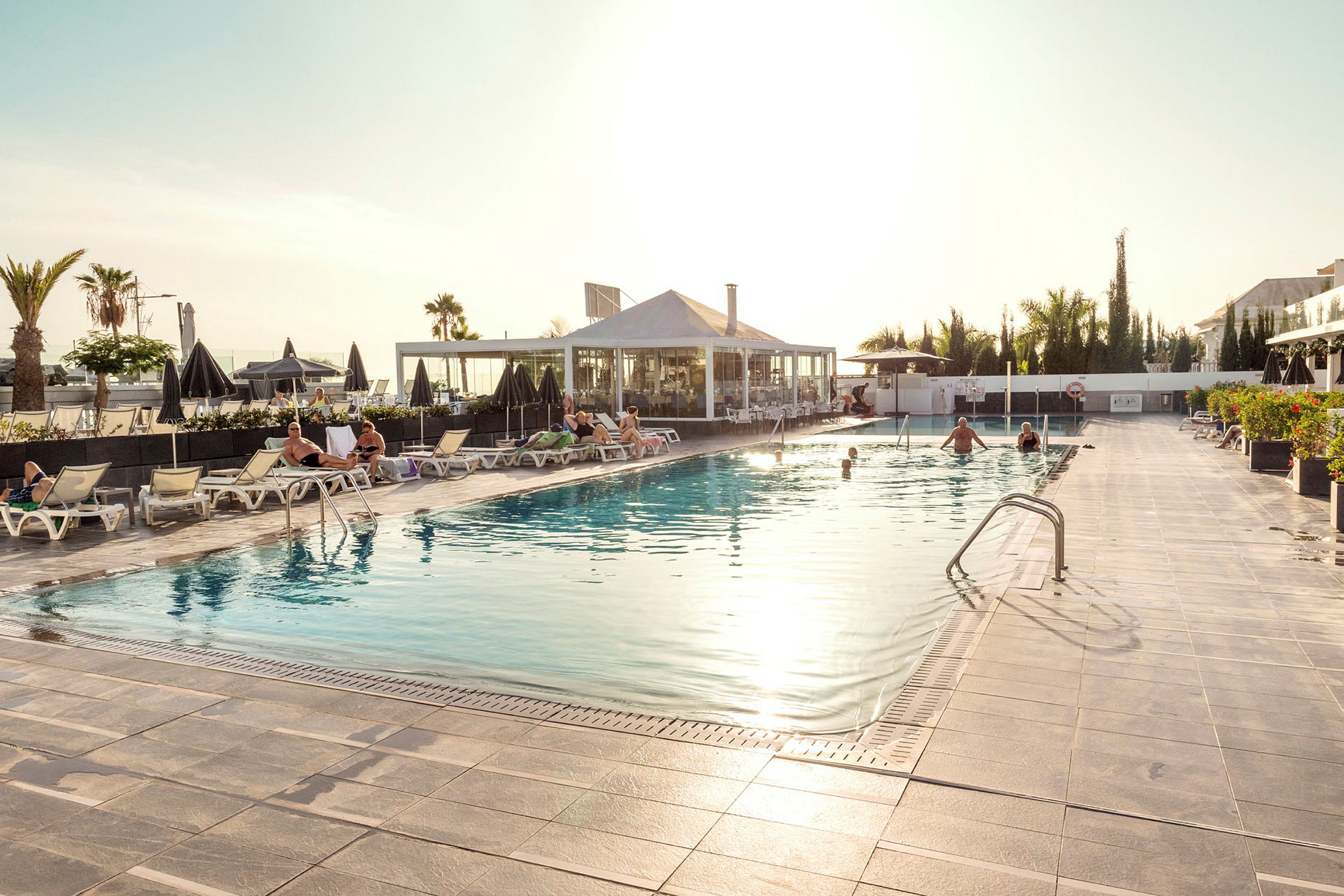 En udendørs pool med liggestole omkring og mennesker, der nyder poolen og området. (AI-genereret tekst)