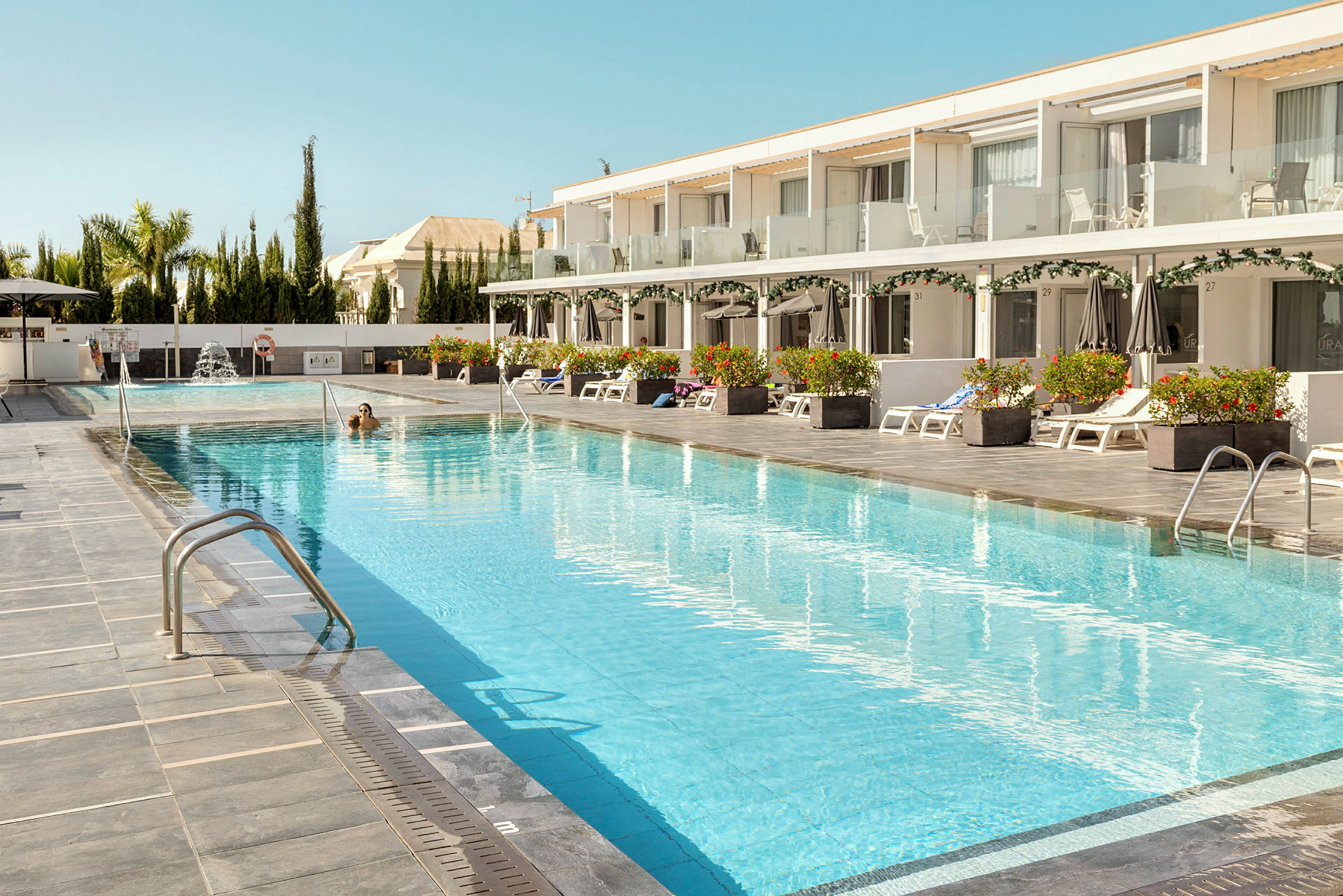 En hotelpool med liggestole og parasoller ved siden af. (AI-genereret tekst)