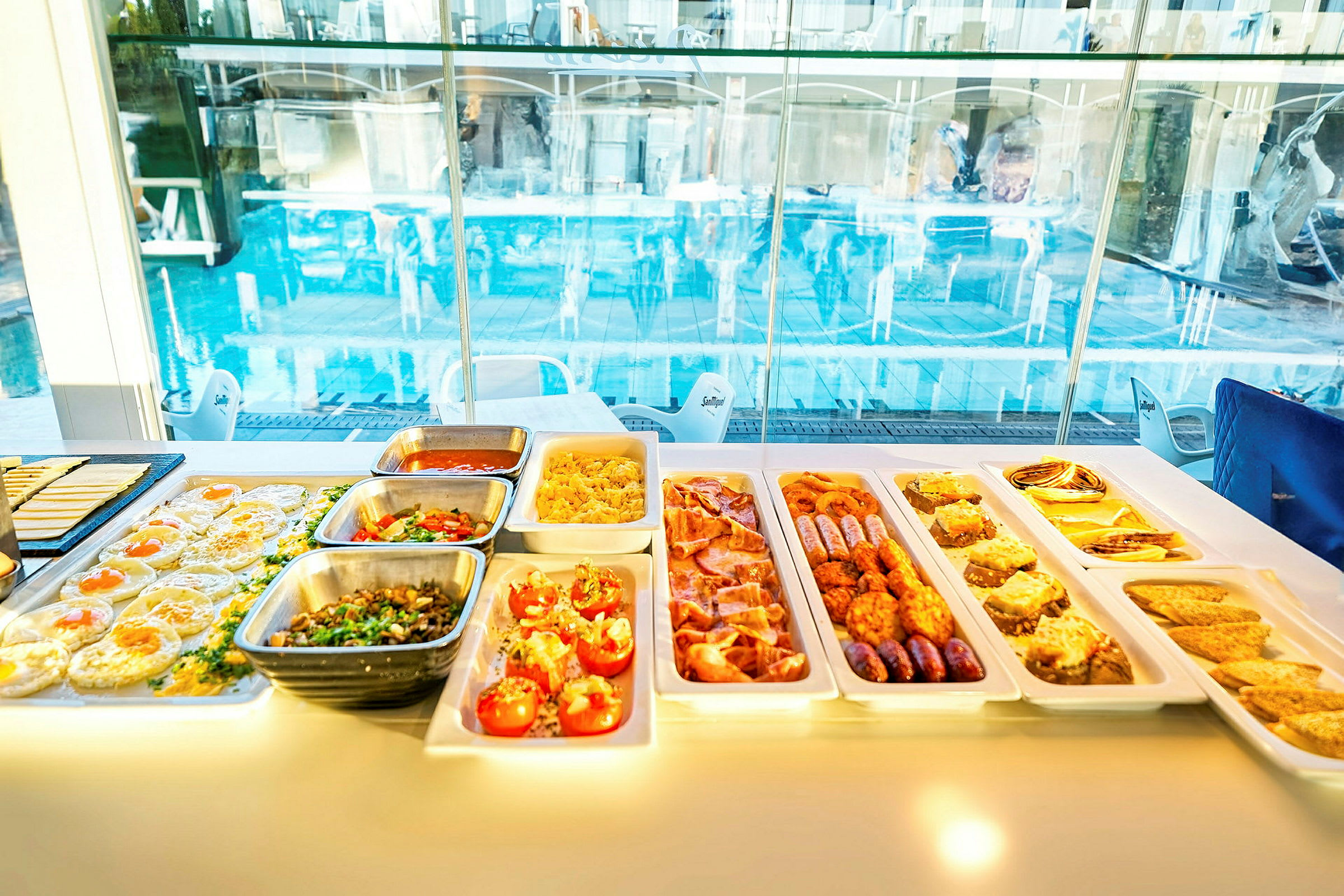 Buffet med forskellige retter ved et vindue med udsigt til en pool. (AI-genereret tekst)