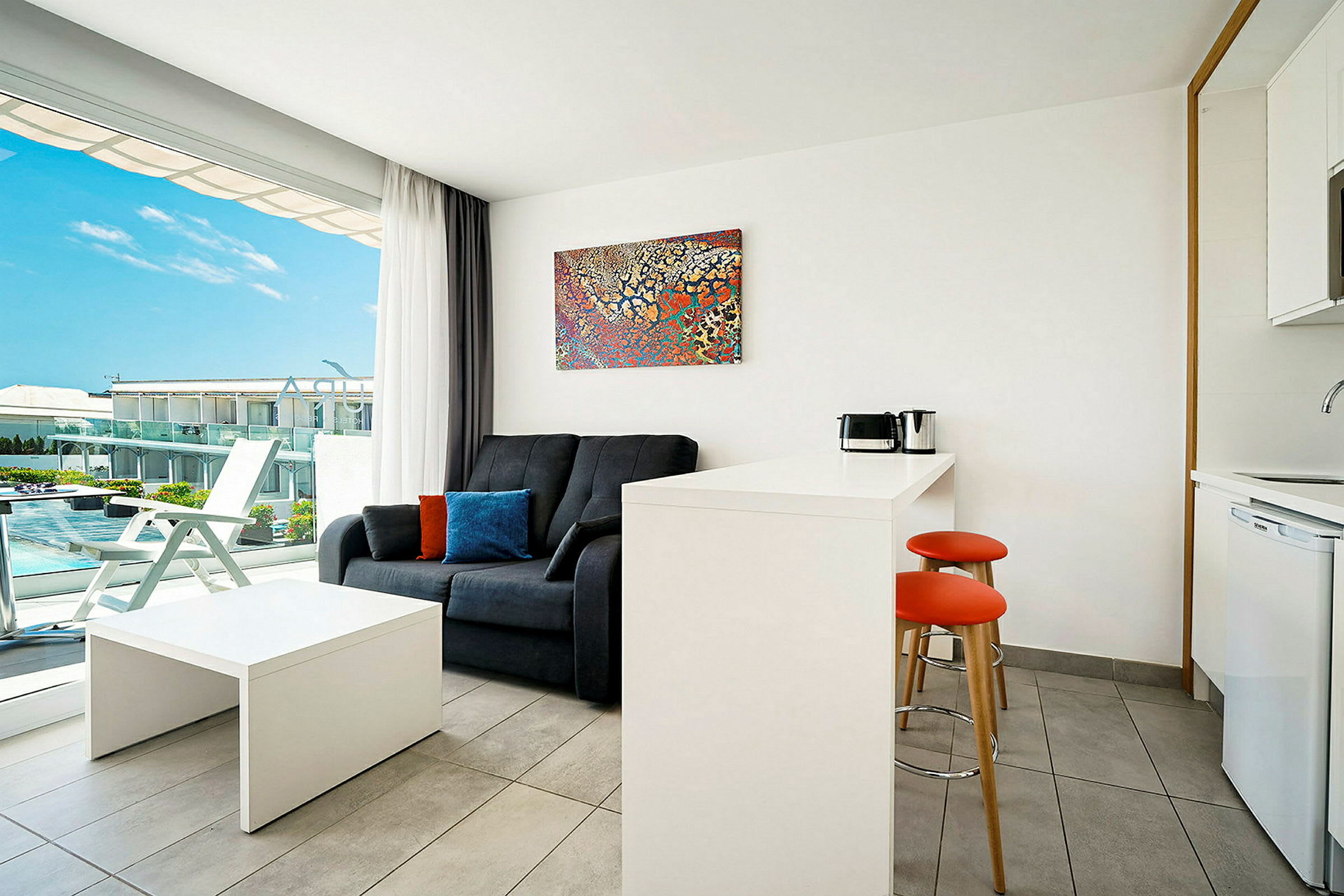 Et moderne hotelværelse med sofa, bord, tekøkken og en balkon med udsigt. (AI-genereret tekst)